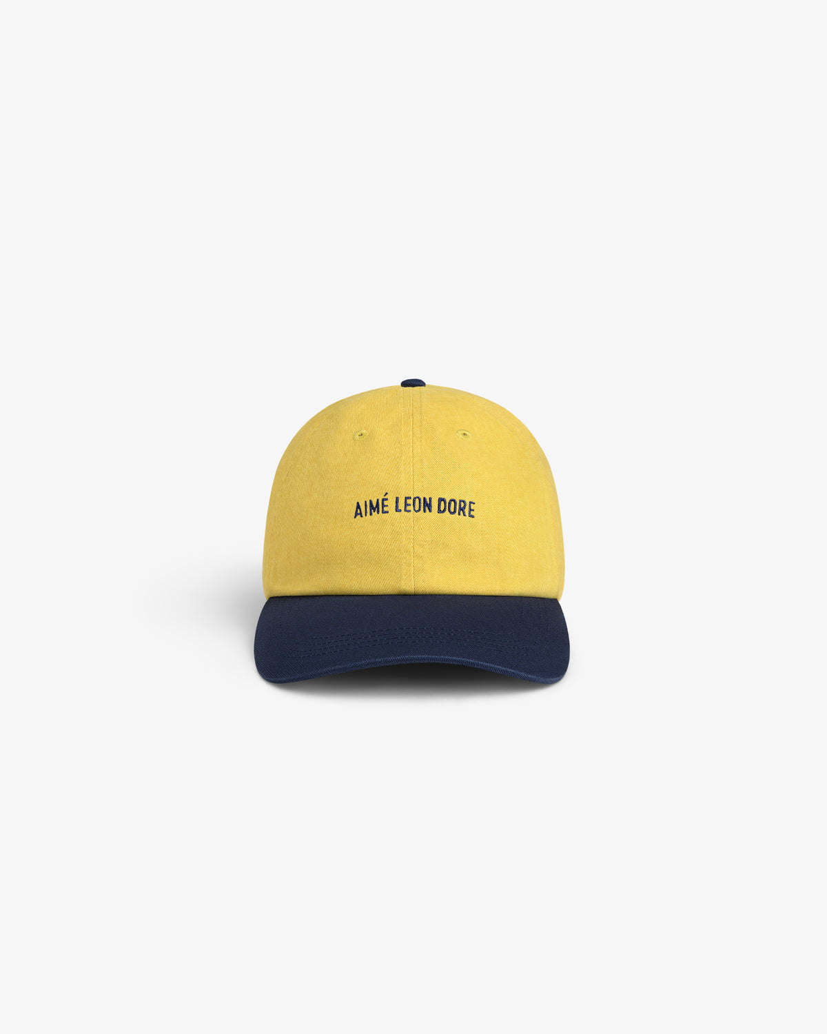 Pigment Dyed Logo Hat: yellow cap with AIMÉ LEON DORE front text and dark blue curved brim, on white background.