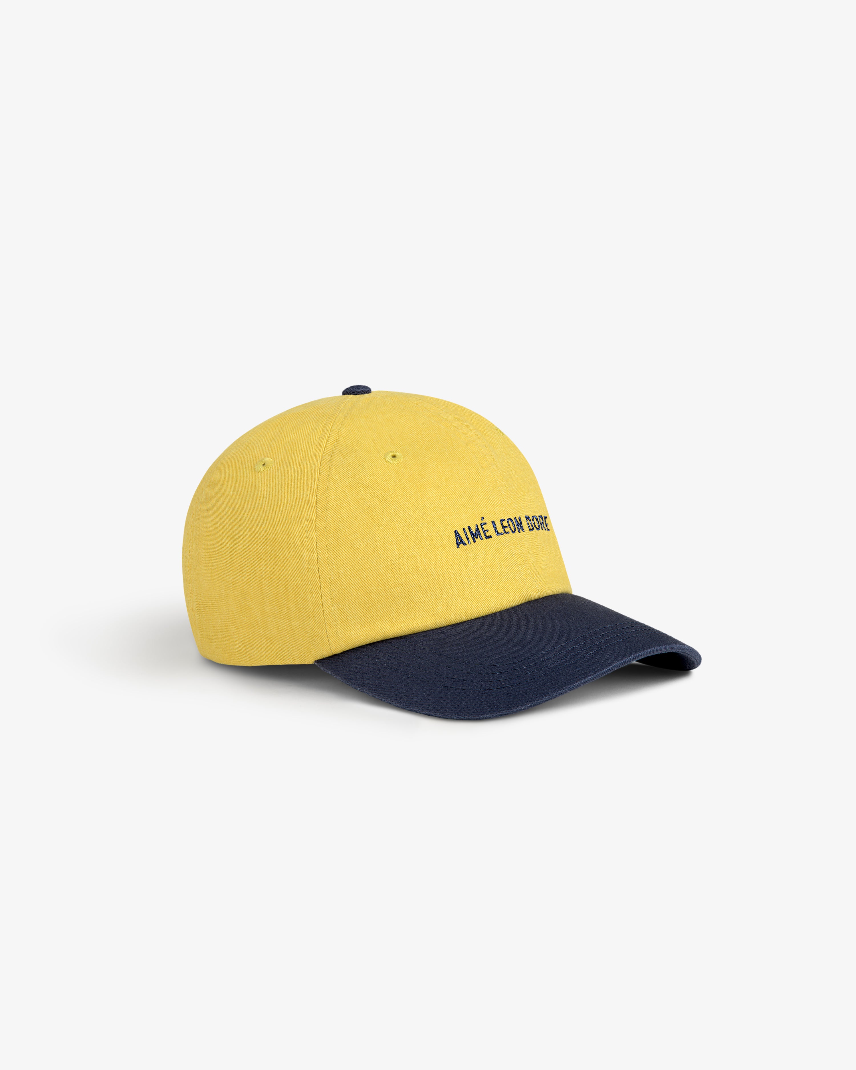 Pigment Dyed Logo Hat: yellow cap with navy brim and AIMÉ LEON DORE embroidered on the front.