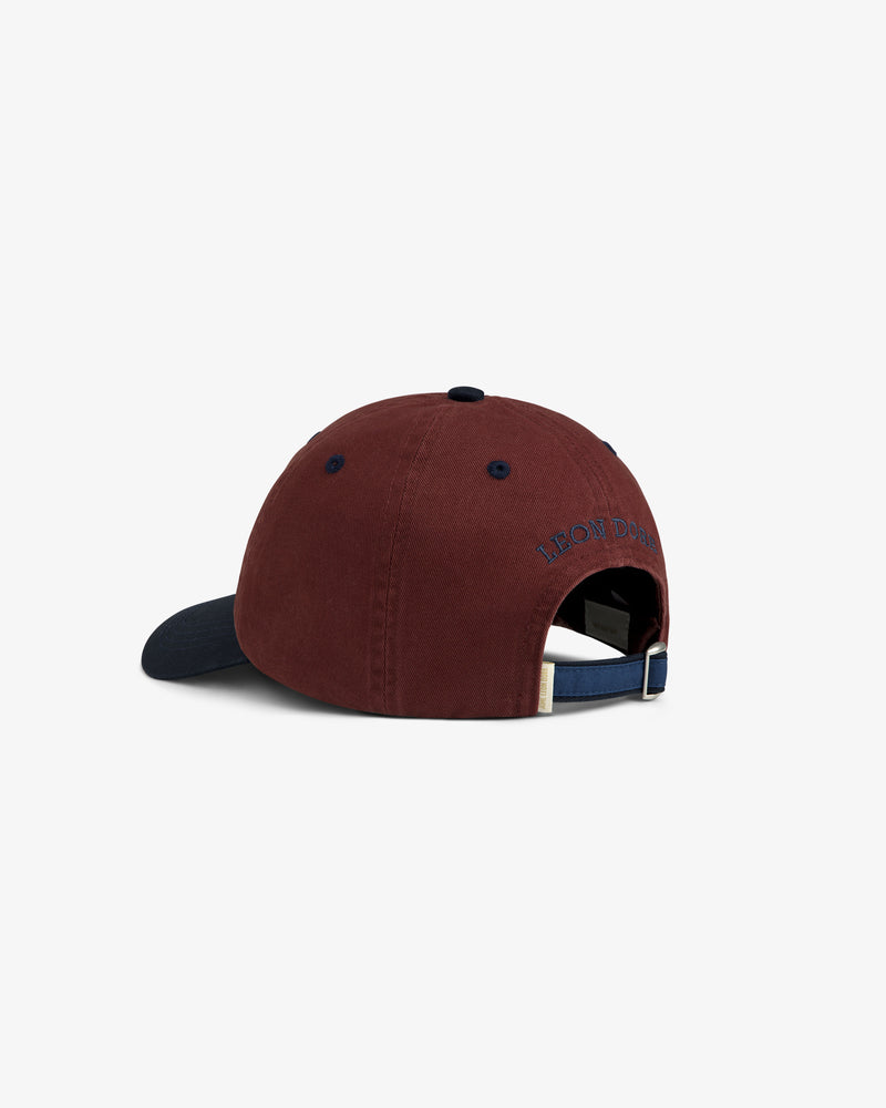 Crest Shield Hat: maroon baseball cap with navy brim, adjustable strap, and embroidered text above the back opening.