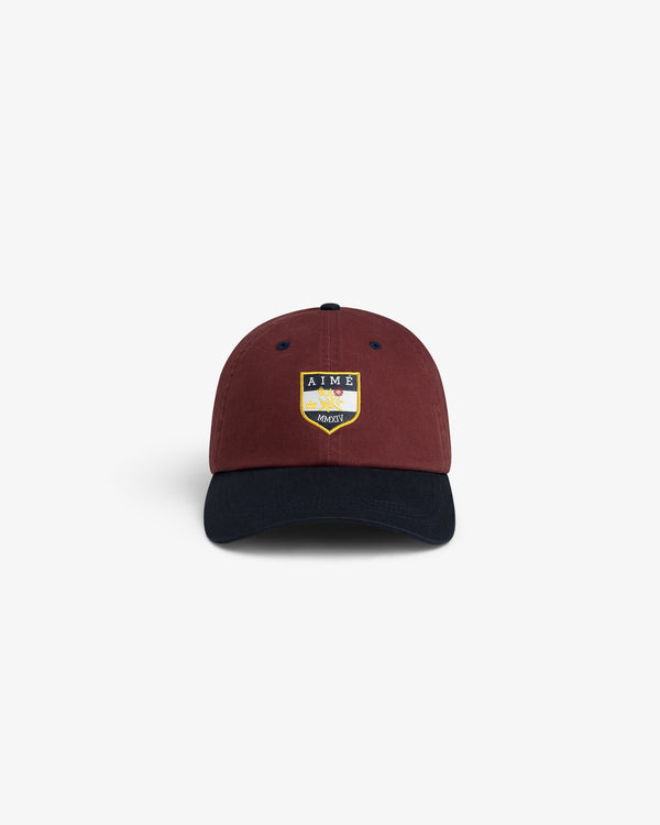 Crest Shield Hat in maroon with navy brim and yellow embroidered AIME crest, shown on a white background.
