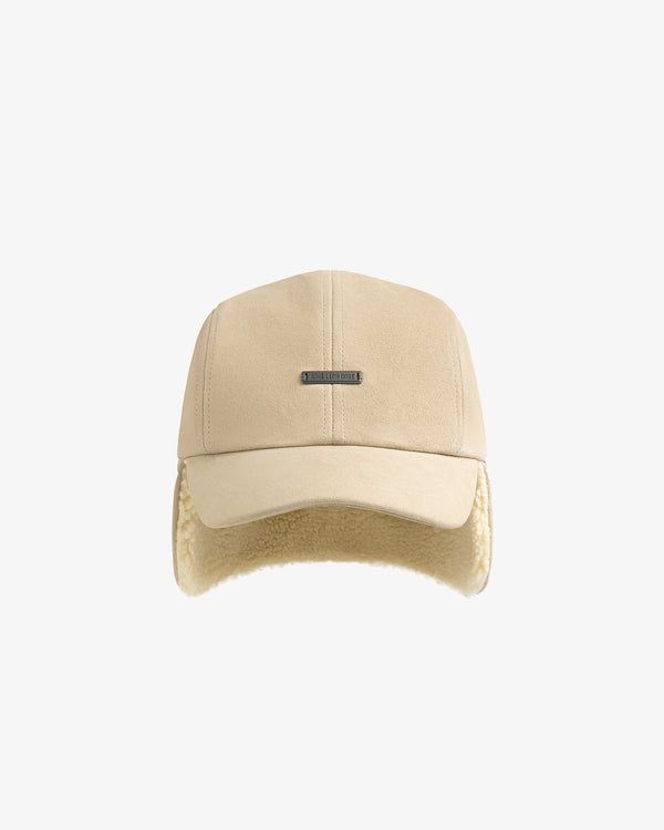 Beige suede Shearling Earflap Hat with a metal logo plate and fleece-lined earflaps.