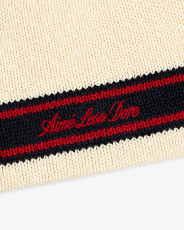 Close-up of the Stripe Knit Beanie in cream with black and red stripes, featuring red Aimé Leon Dore embroidery.