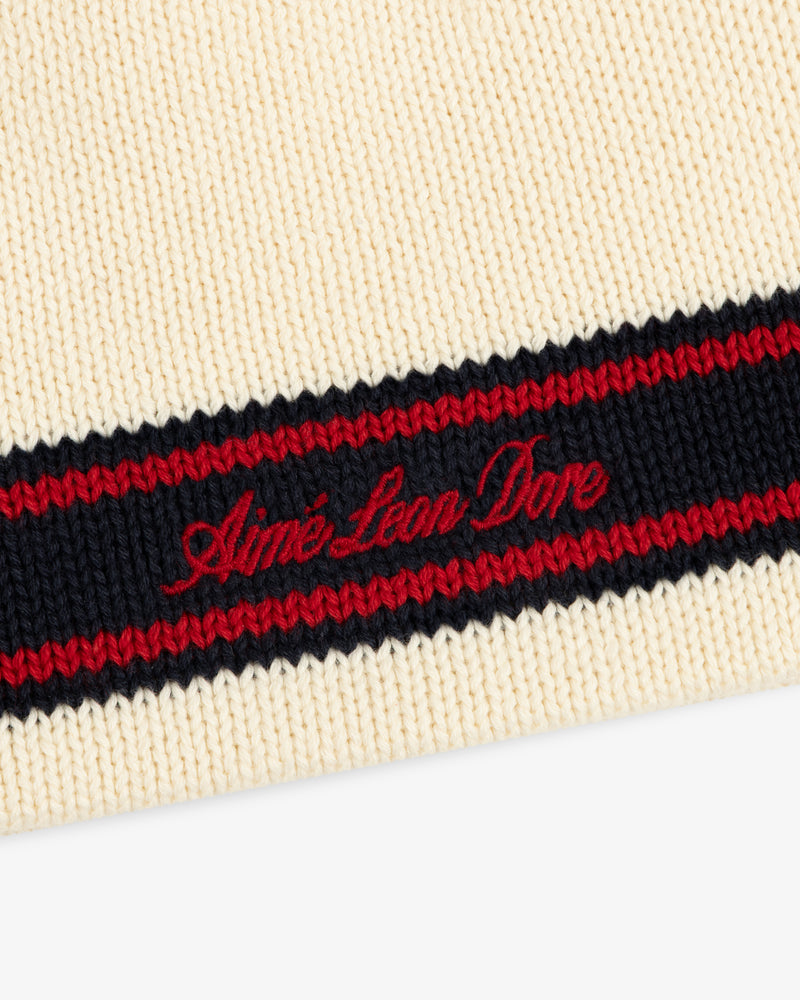 Close-up of the Stripe Knit Beanie in cream with black and red stripes, featuring red Aimé Leon Dore embroidery.
