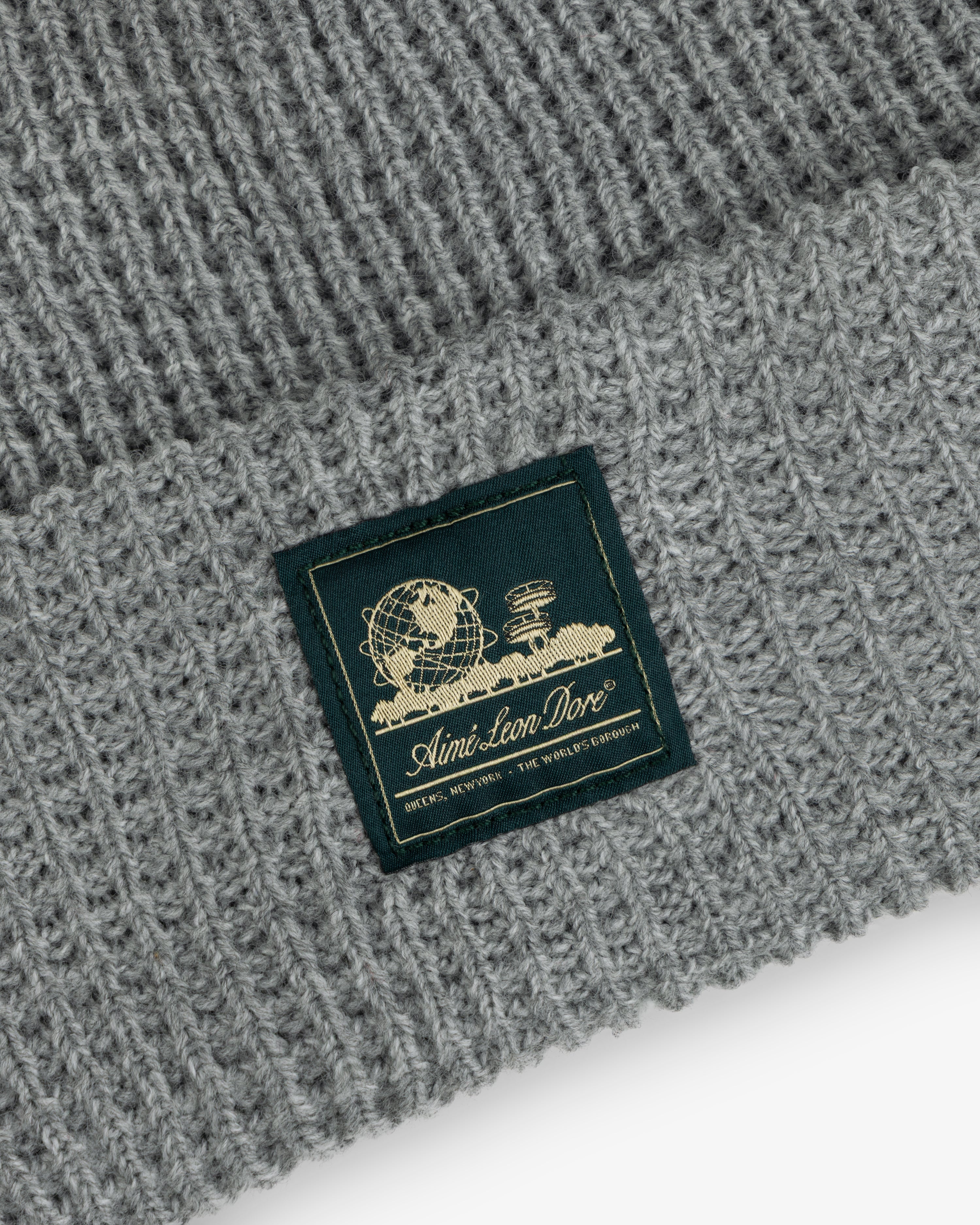Grey Waffle Knit Beanie with a globe, books, and “Aimé Leon Dore” in gold on a woven patch.