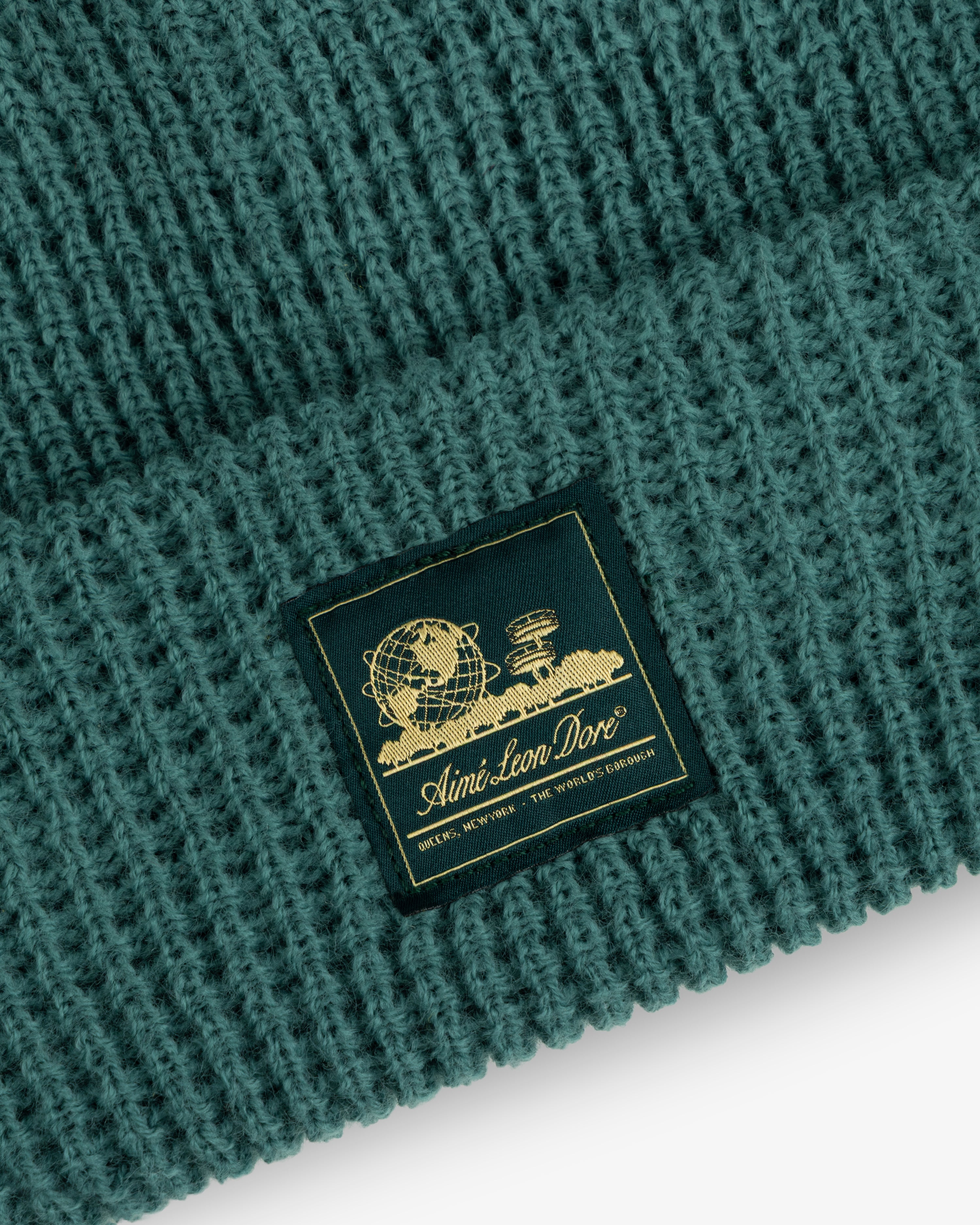 Close-up of a green Waffle Knit Beanie with a black and gold Aimé Leon Dore patch on the front.
