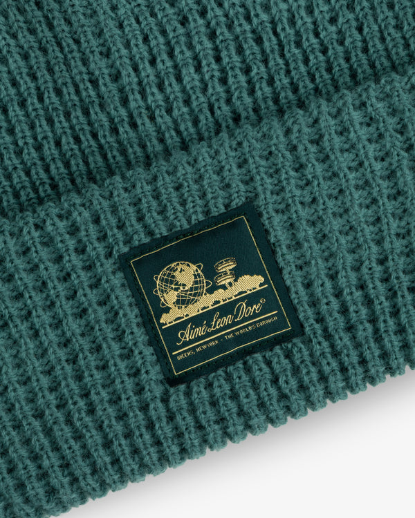 Close-up of a green Waffle Knit Beanie with a black and gold Aimé Leon Dore patch on the front.