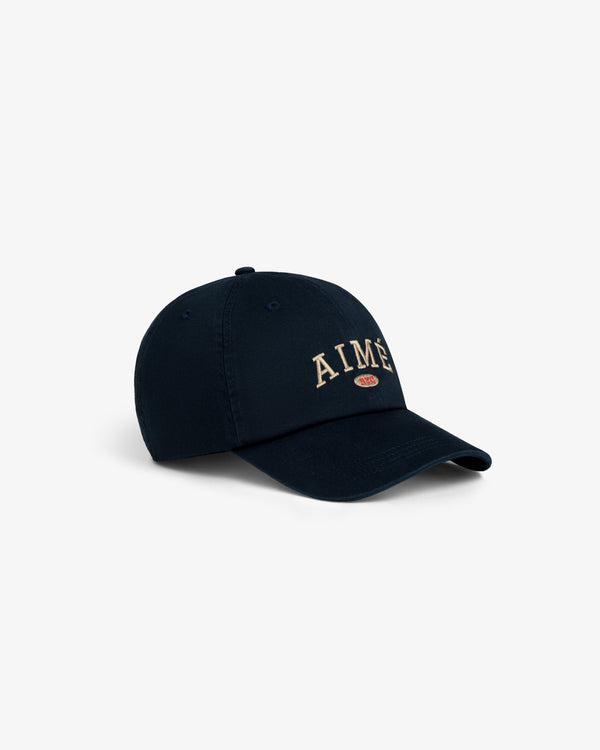 Aimé Souvenir Hat: Navy cap with beige AIMÉ embroidery and a small red oval logo beneath the text on the front.