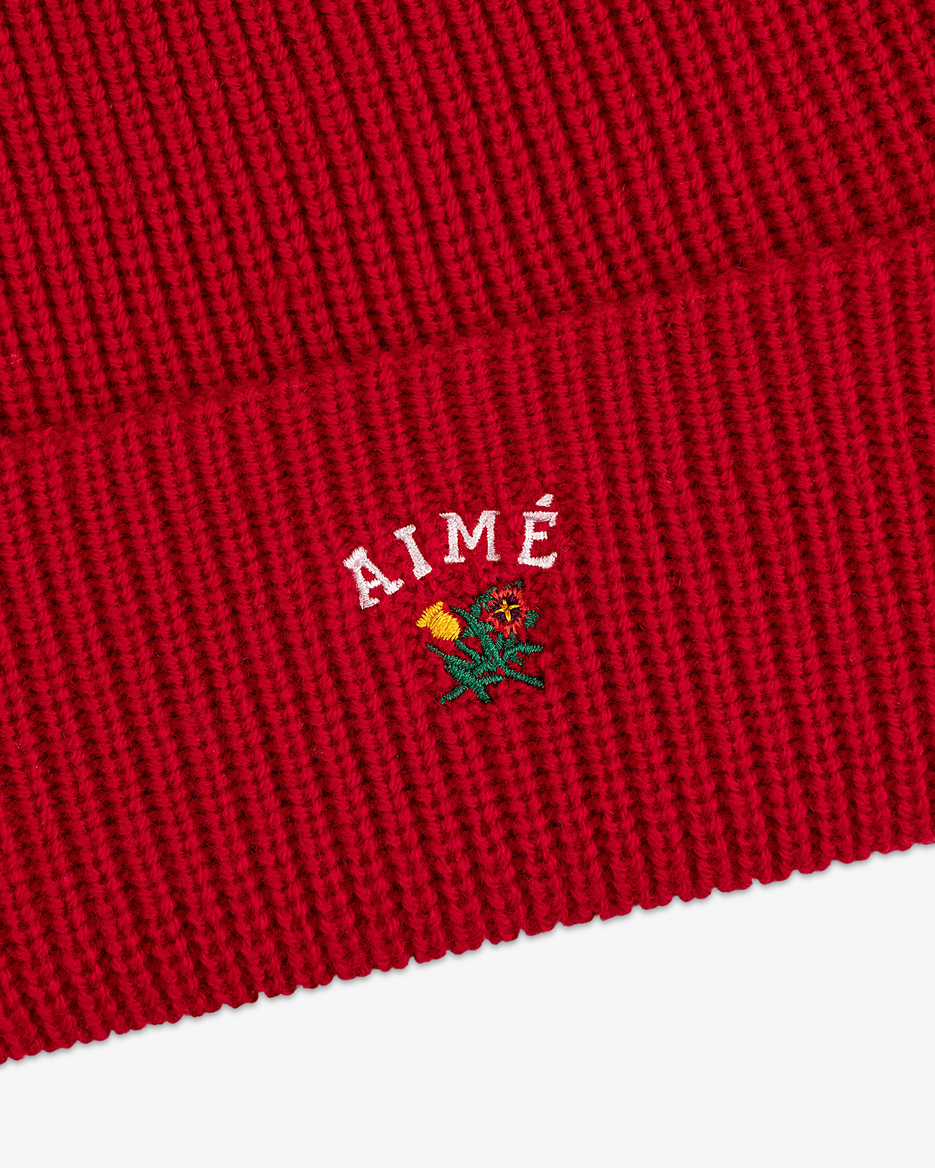 Crest Merino Wool Beanie: Red ribbed knit with AIMÉ and a small yellow and green embroidered flower.