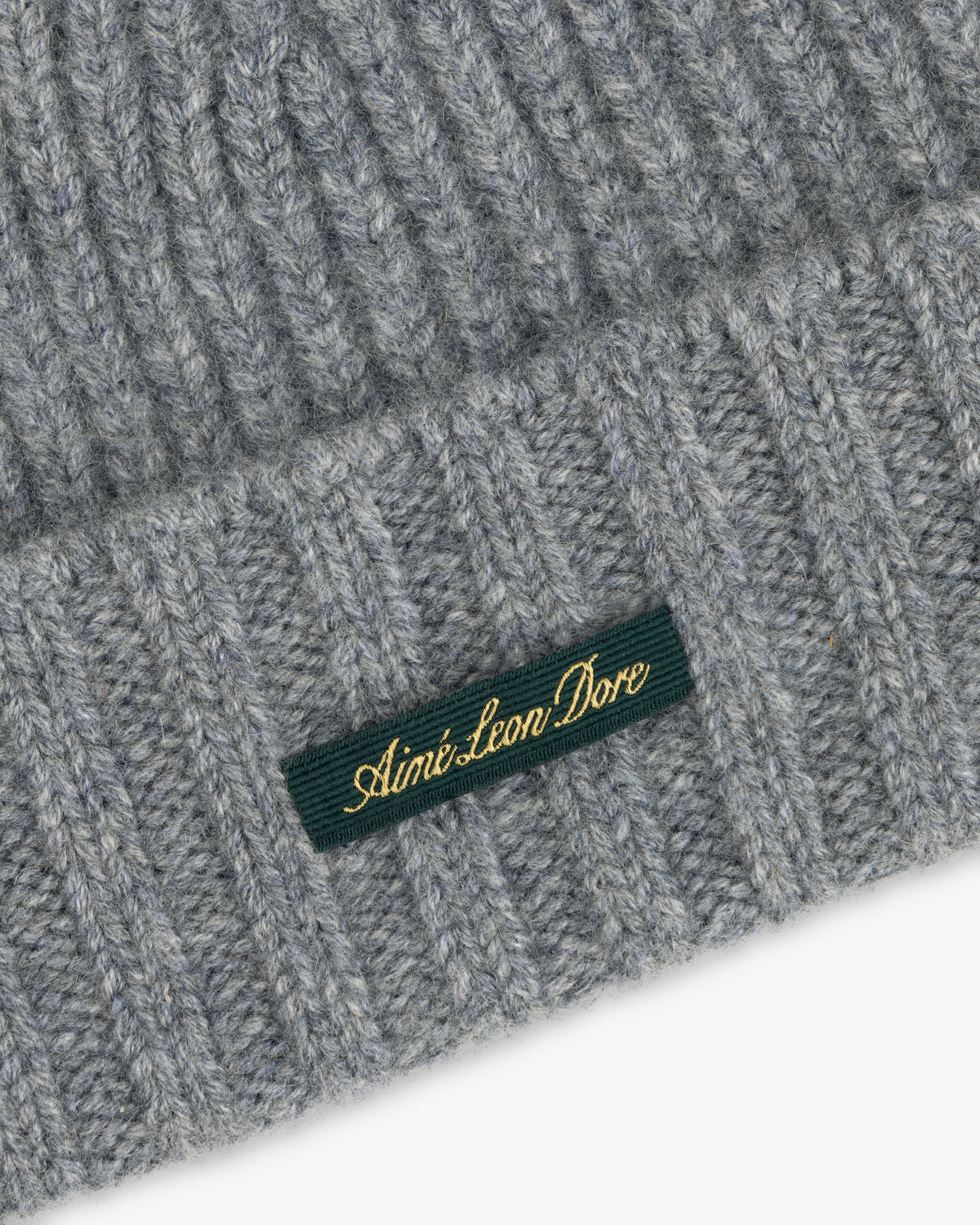 Grey ribbed knit Cashmere Beanie with a green woven tag featuring gold text.