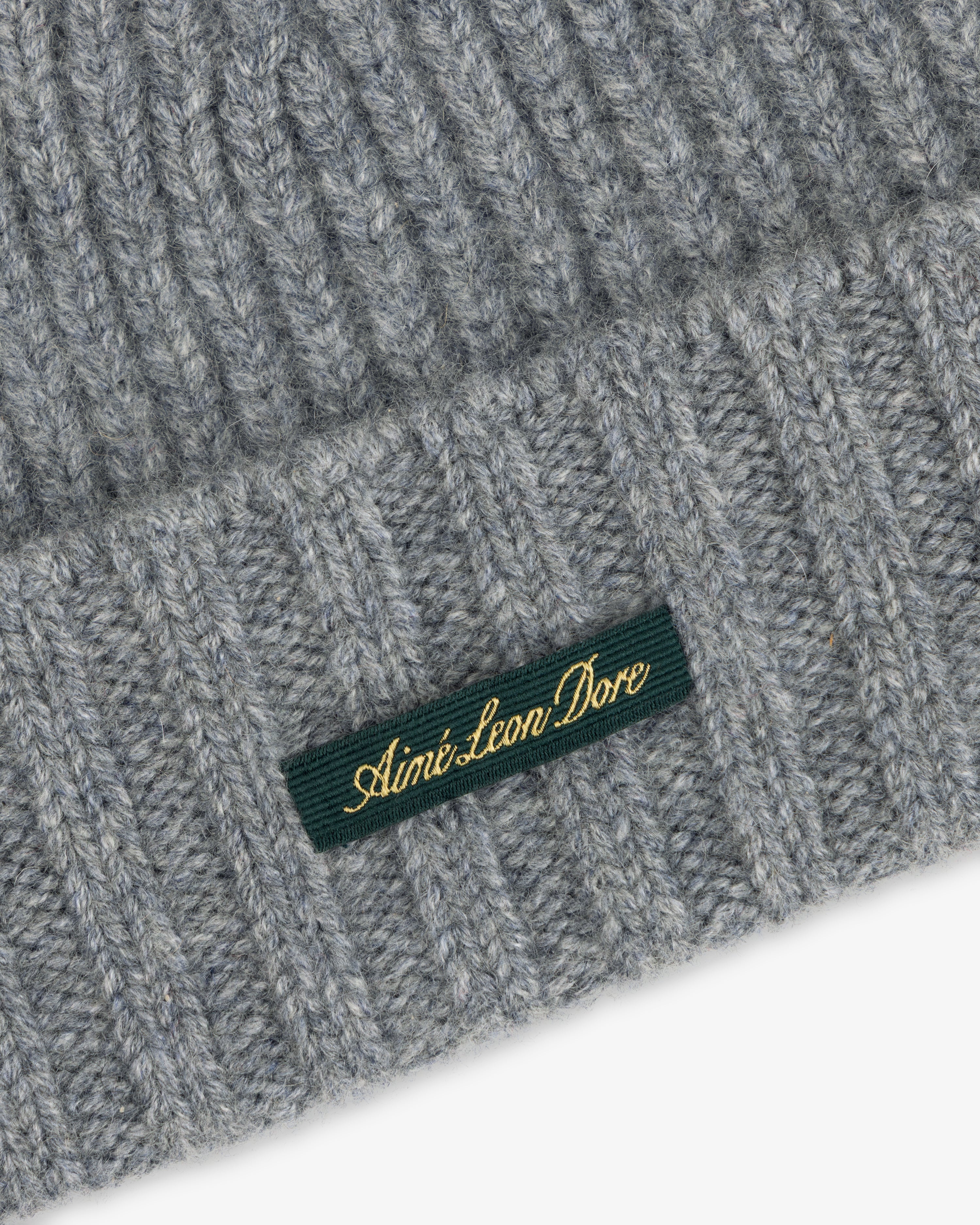 Grey ribbed knit Cashmere Beanie with a green woven tag featuring gold text.