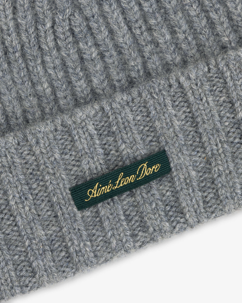 Grey ribbed knit Cashmere Beanie with a green woven tag featuring gold text.