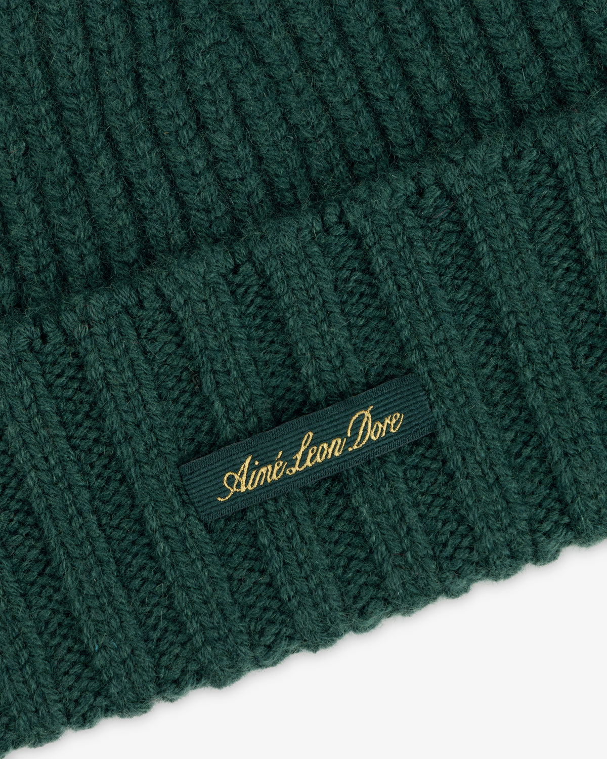 Dark green ribbed knit Cashmere Beanie with a small tag embroidered with Aimé Leon Dore in gold thread.