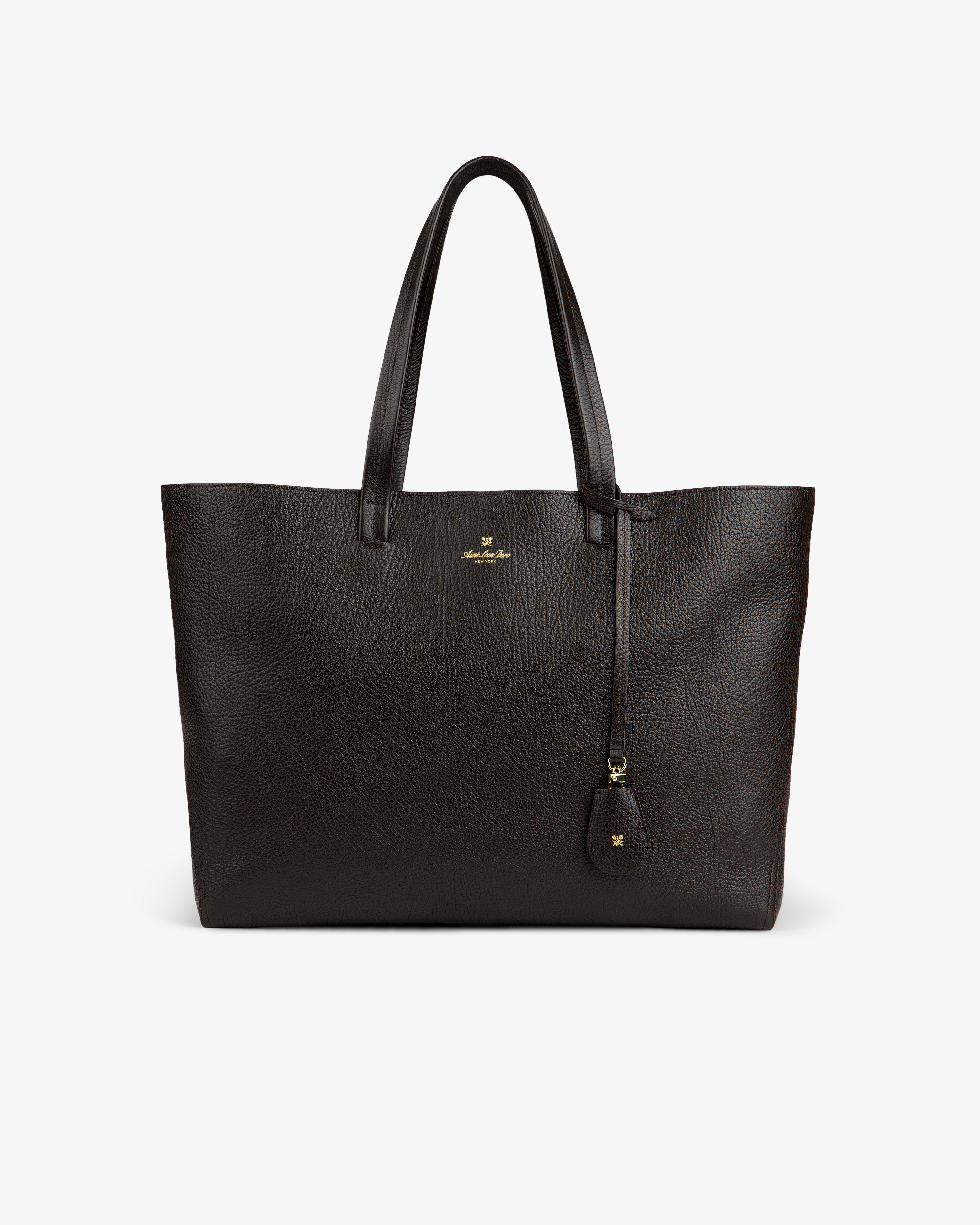 The Tumbled Leather Tote Bag is large, dark brown with two handles and a small gold logo on the front.