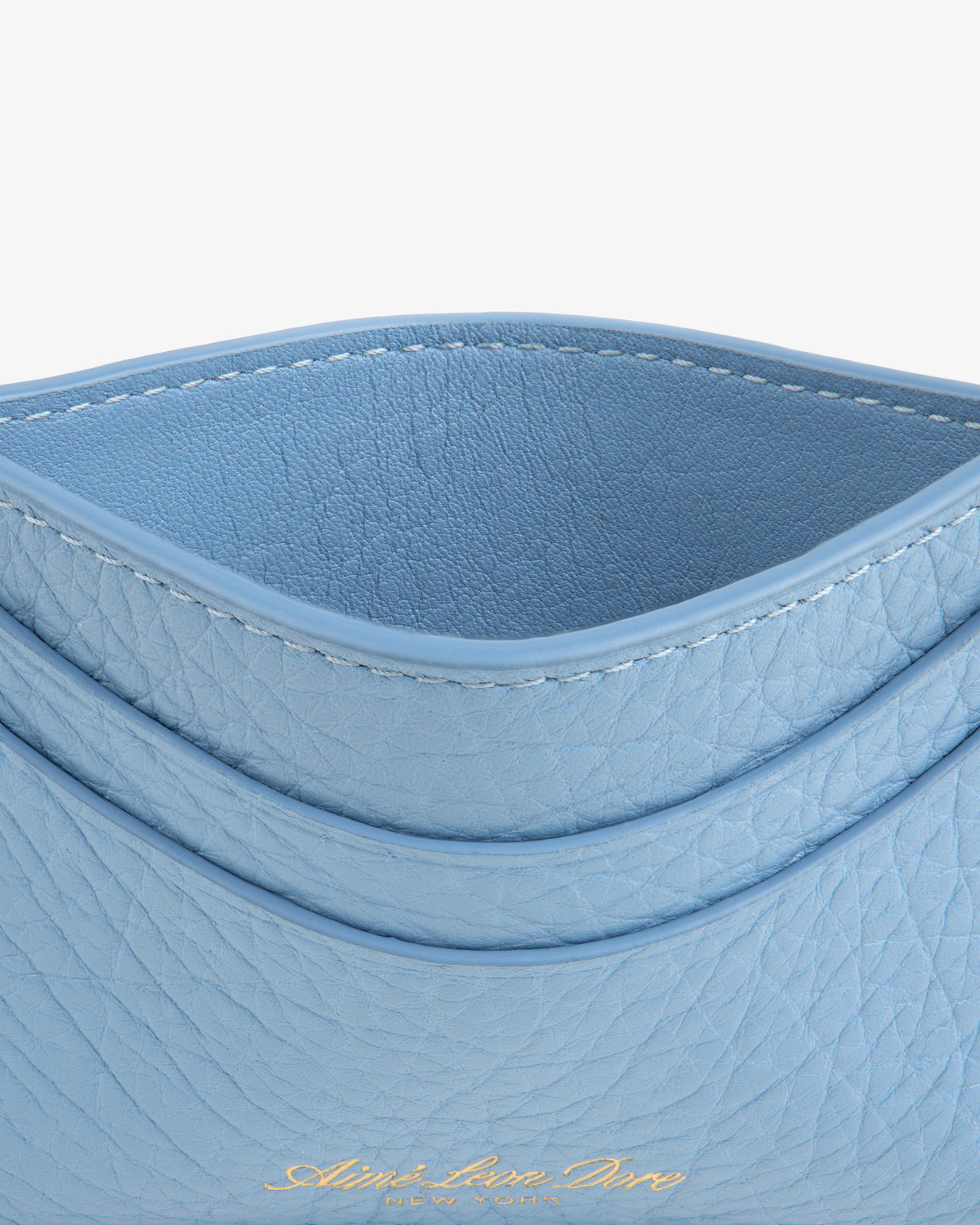 A close-up of the Tumbled Leather Card Holder in light blue leather with gold embossed text at the bottom.