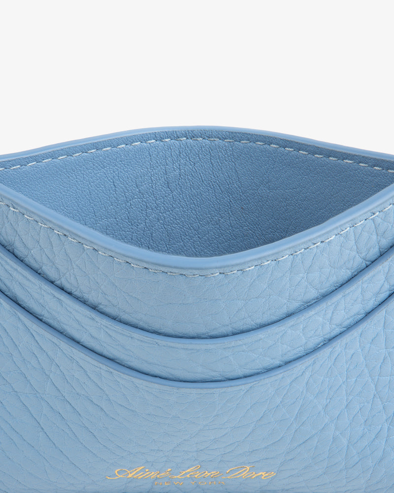 A close-up of the Tumbled Leather Card Holder in light blue leather with gold embossed text at the bottom.