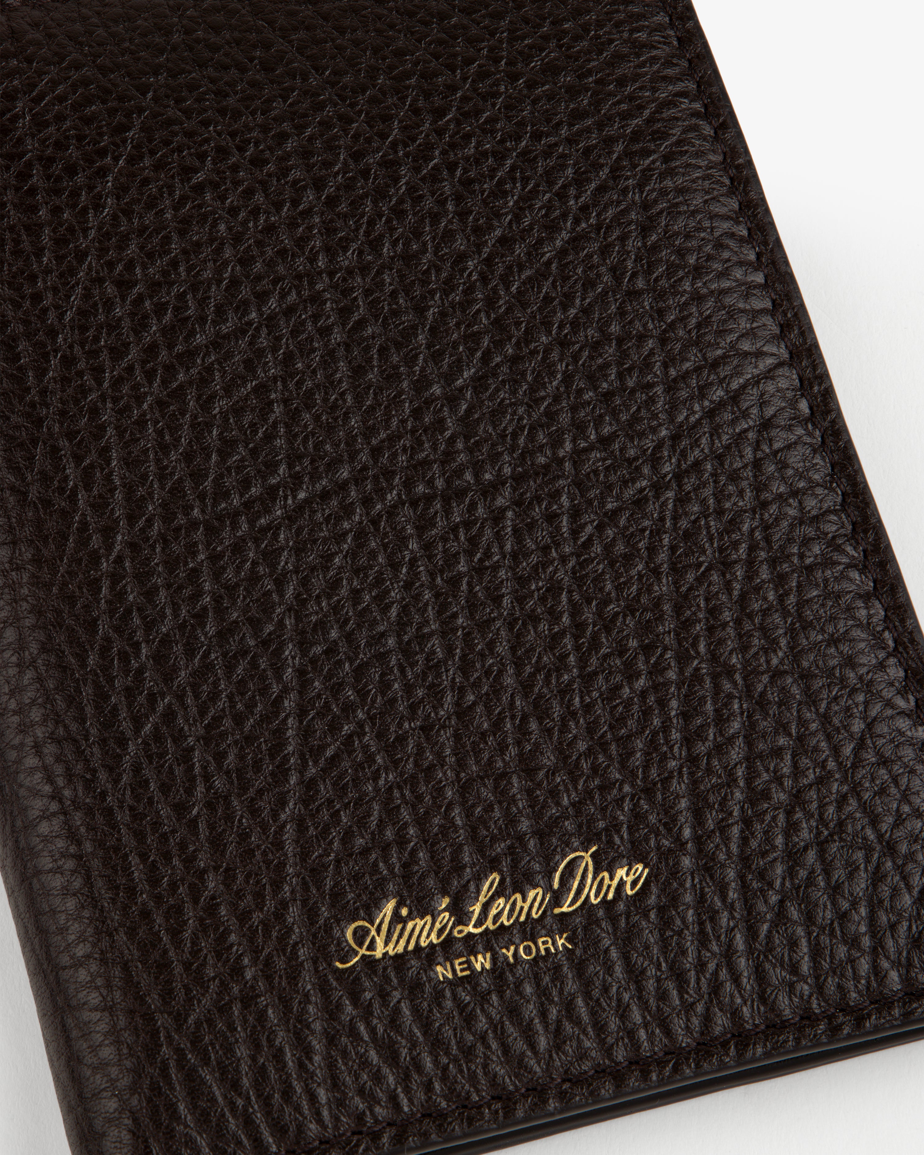 Close-up of a black Tumbled Leather Passport Holder with Aimé Leon Dore New York embossed in gold near the bottom.