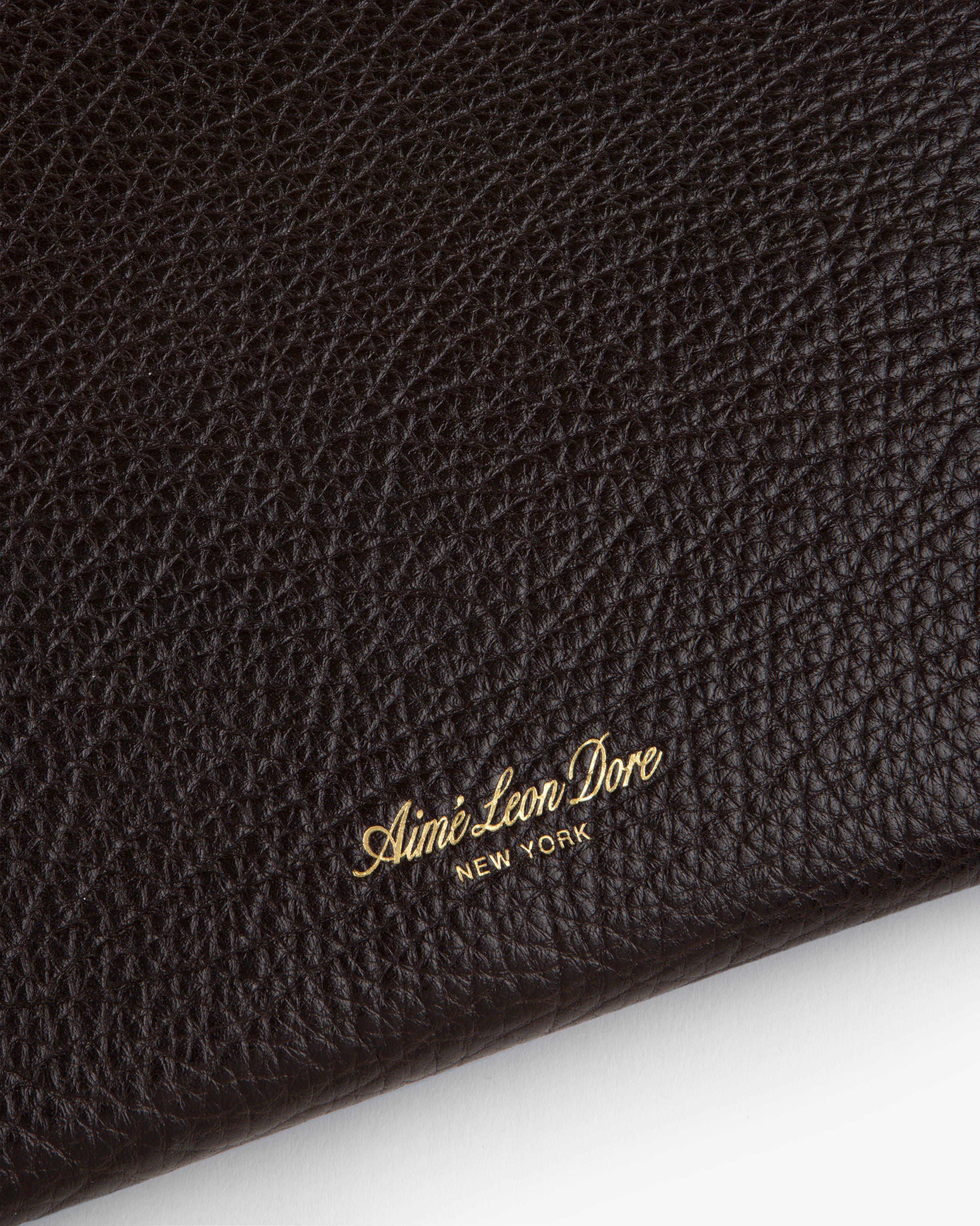 Close-up of black tumbled leather Small Pouch with gold Aimé Leon Dore NEW YORK embossed in the corner.