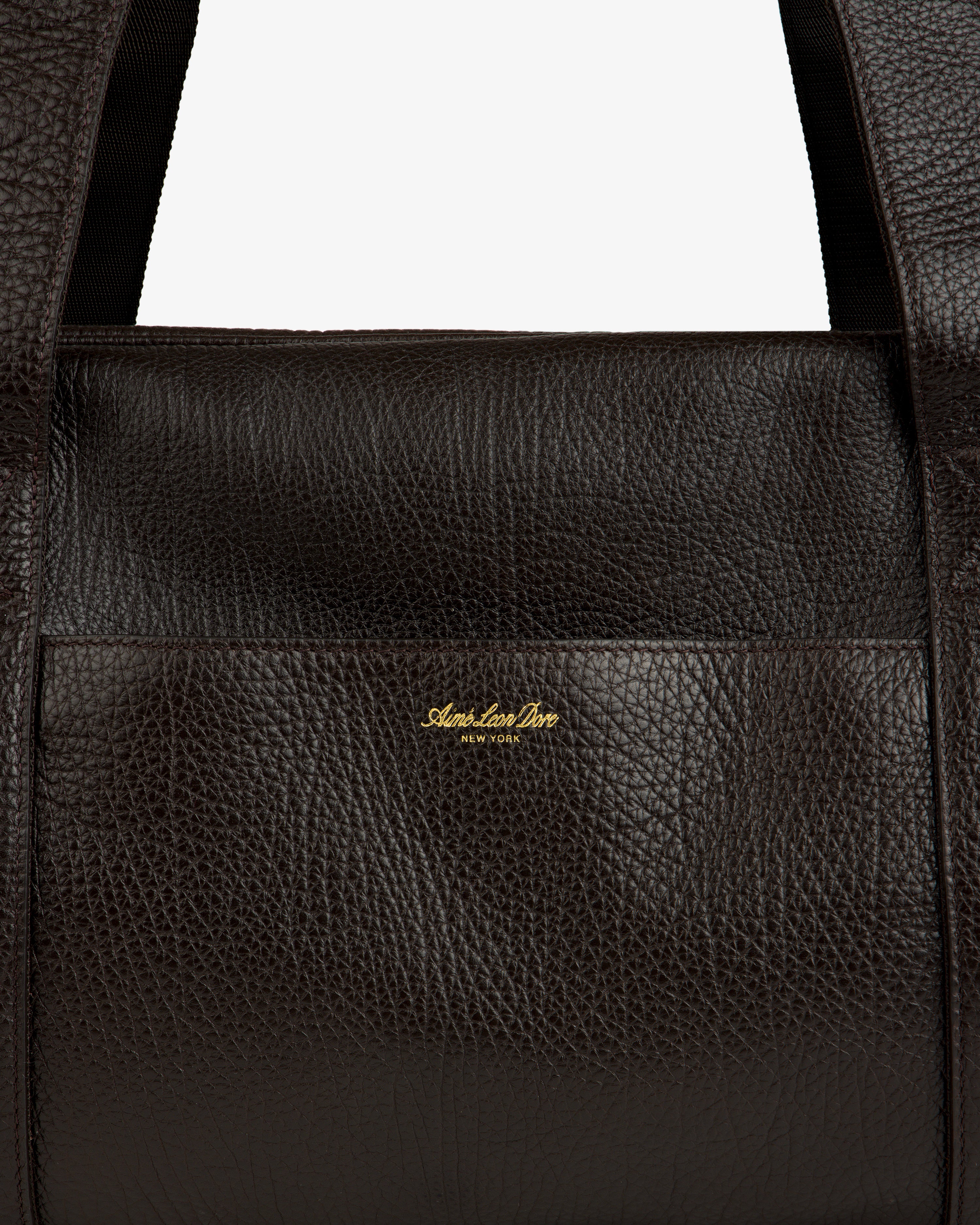 Close-up of Tumbled Leather Duffle in dark brown with visible grain and gold Aimé Leon Dore New York logo on front.