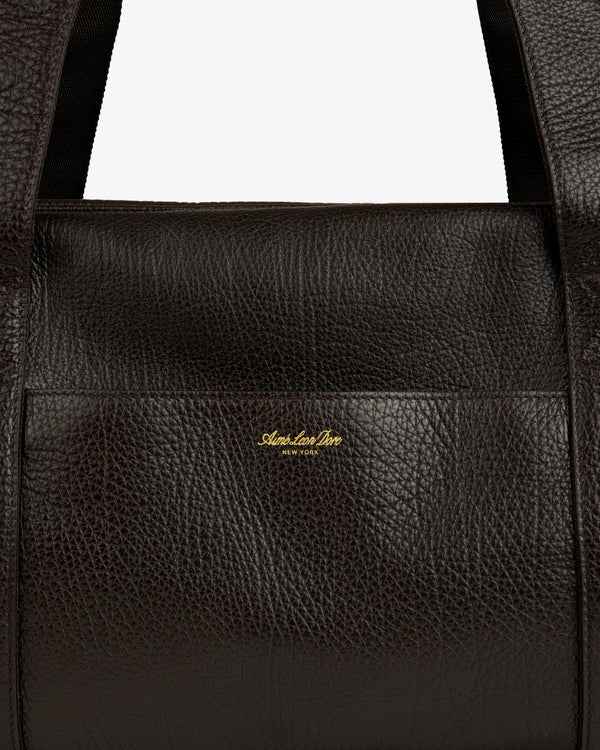 Close-up of Tumbled Leather Duffle in dark brown with visible grain and gold Aimé Leon Dore New York logo on front.