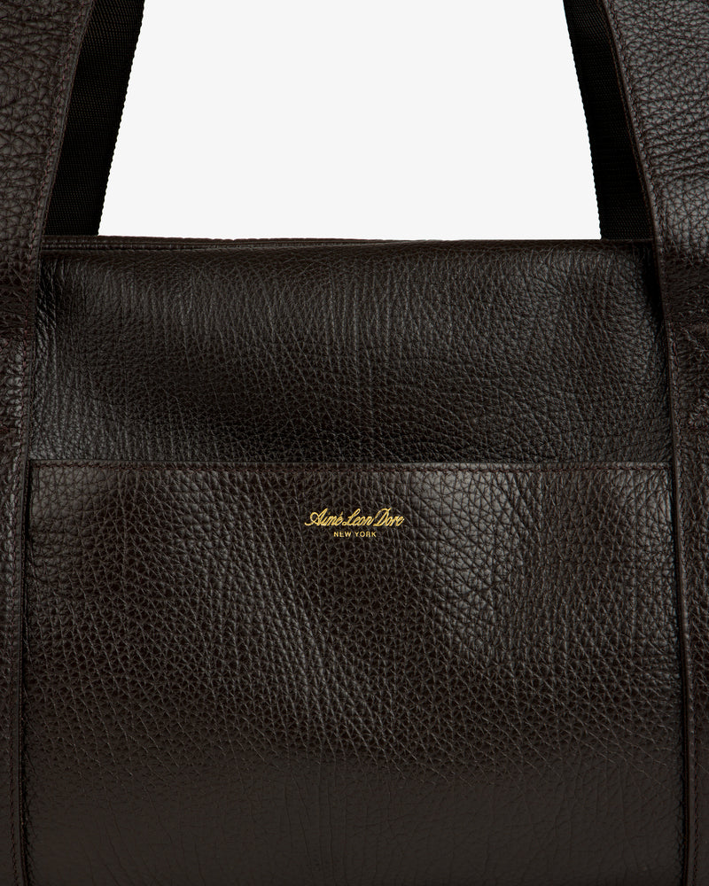 Close-up of Tumbled Leather Duffle in dark brown with visible grain and gold Aimé Leon Dore New York logo on front.