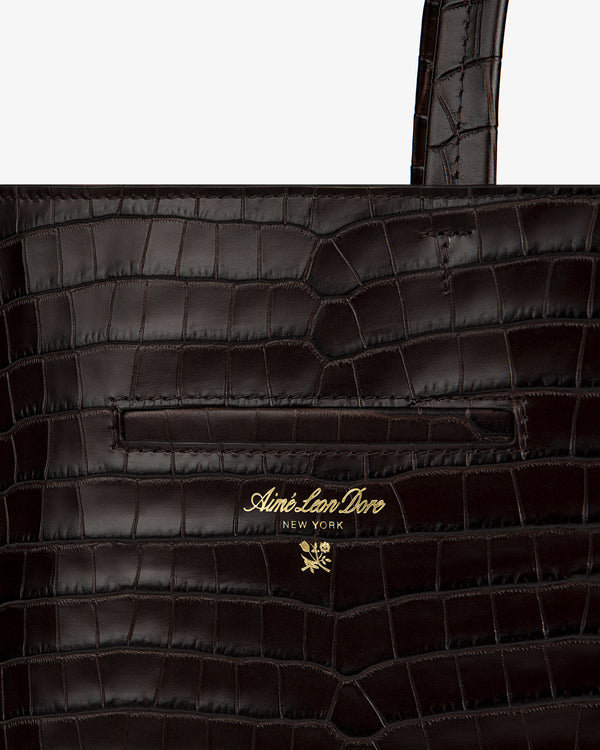 Dark brown croc-embossed leather shoulder bag with a gold-tone brand logo and floral emblem.