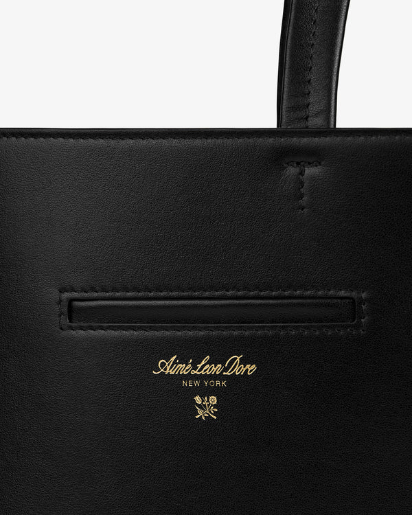 Black Napa Leather Shoulder Bag with gold-colored Aimé Leon Dore New York text above a small floral icon.