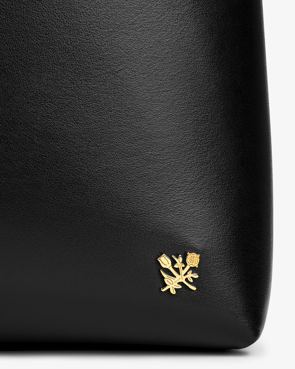 Close-up of a black Napa Leather Shoulder Bag featuring a small gold flower emblem.