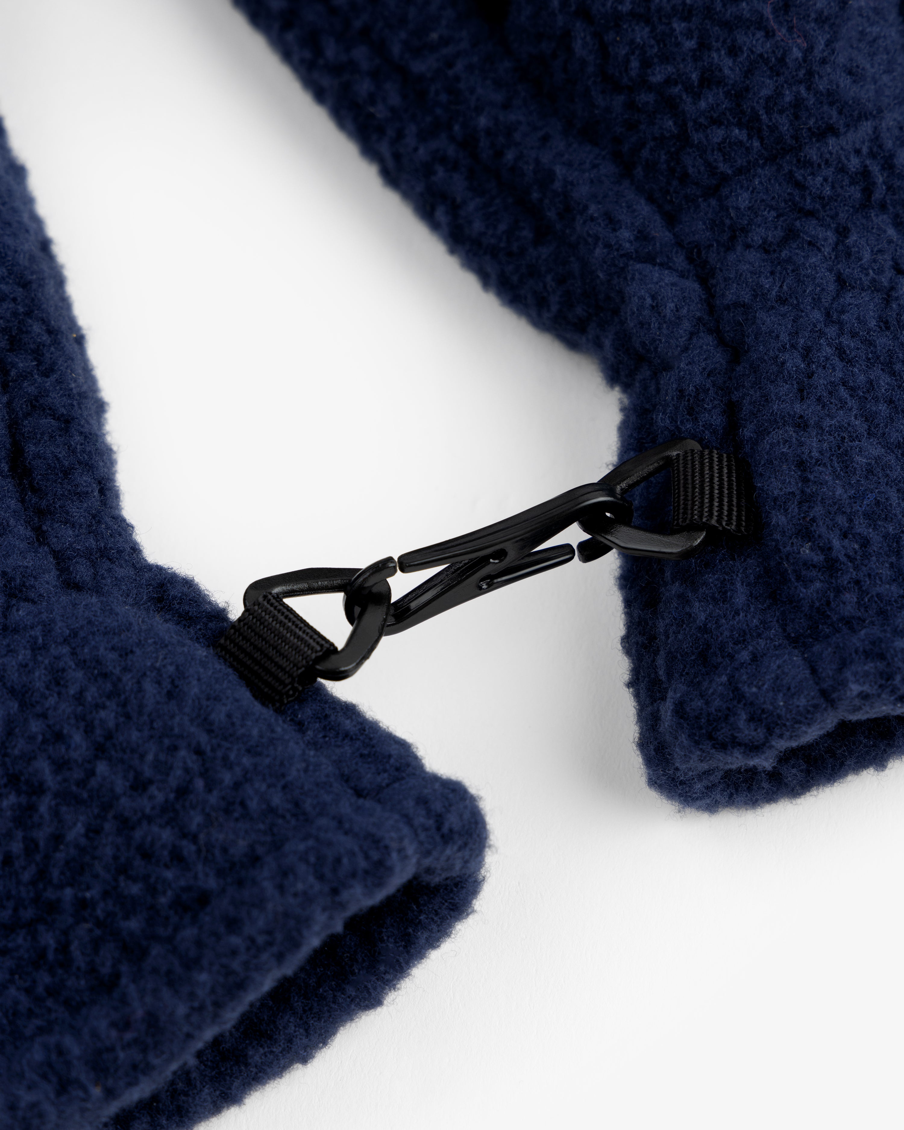 Close-up of a black clip joining two navy fleece ALD / The North Face Fleece Gloves on a white background.