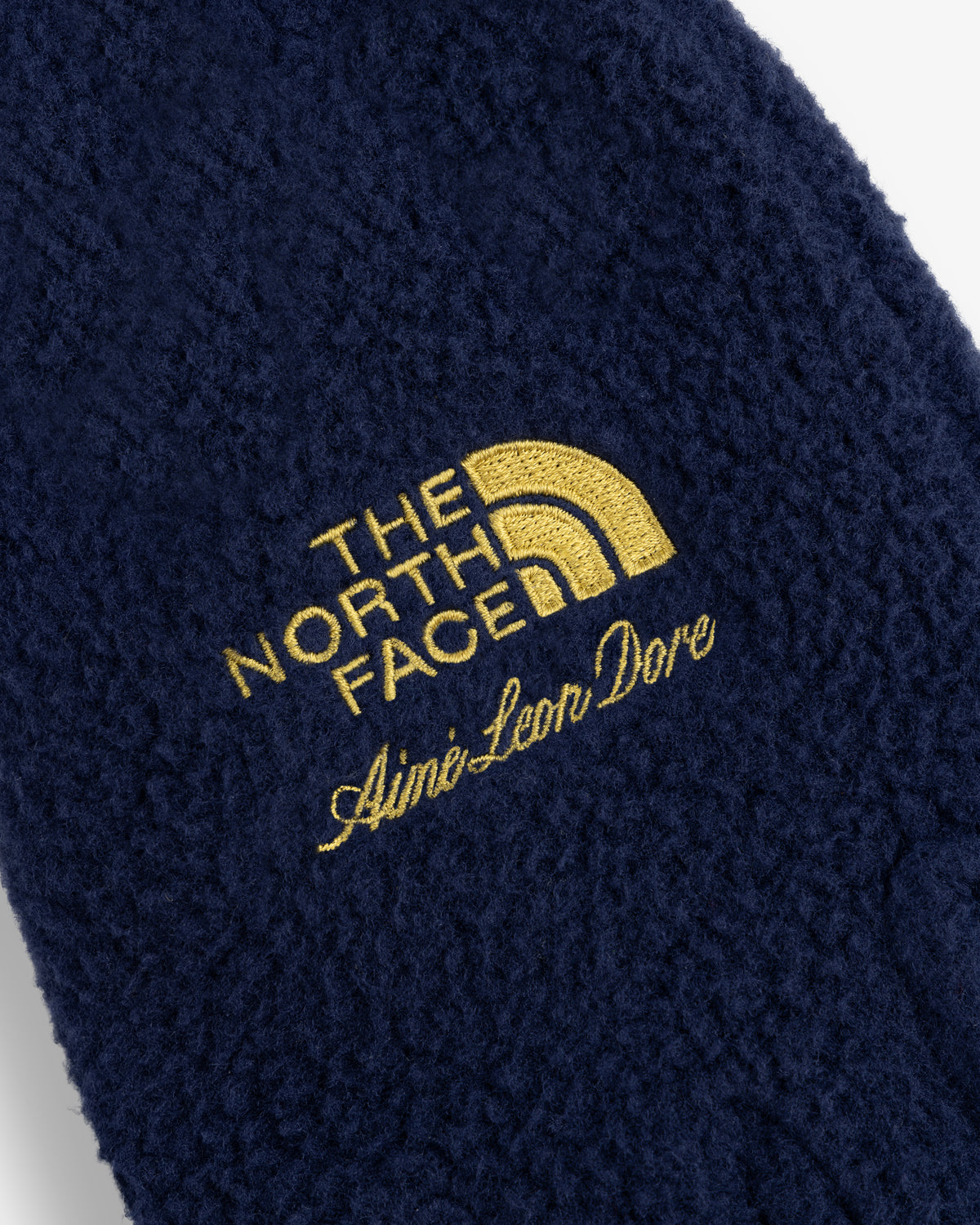 Close-up of ALD / The North Face Fleece Gloves with yellow logos embroidered on navy blue fleece.