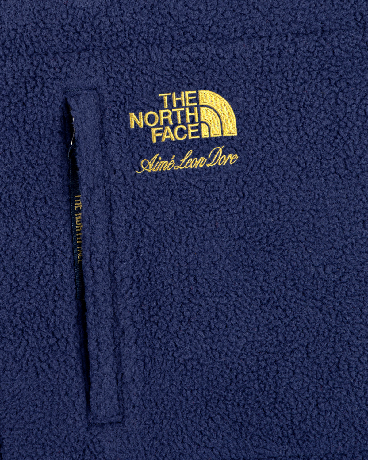 Close-up of a blue ALD / The North Face Denali Fleece Scarf with yellow embroidered logo and zippered pocket.