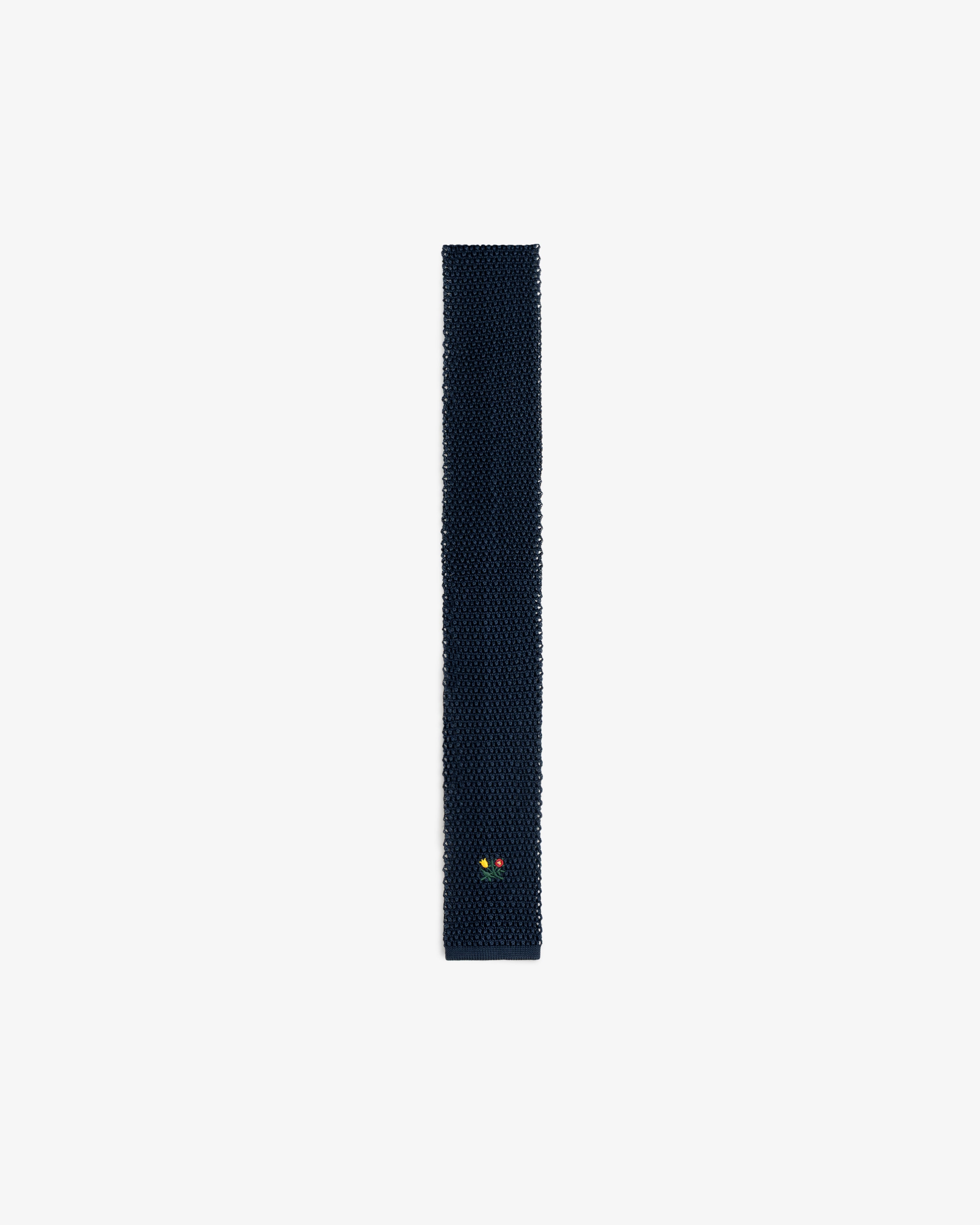 Crest Silk Knit Tie in dark blue with a small yellow and red floral emblem near the bottom.