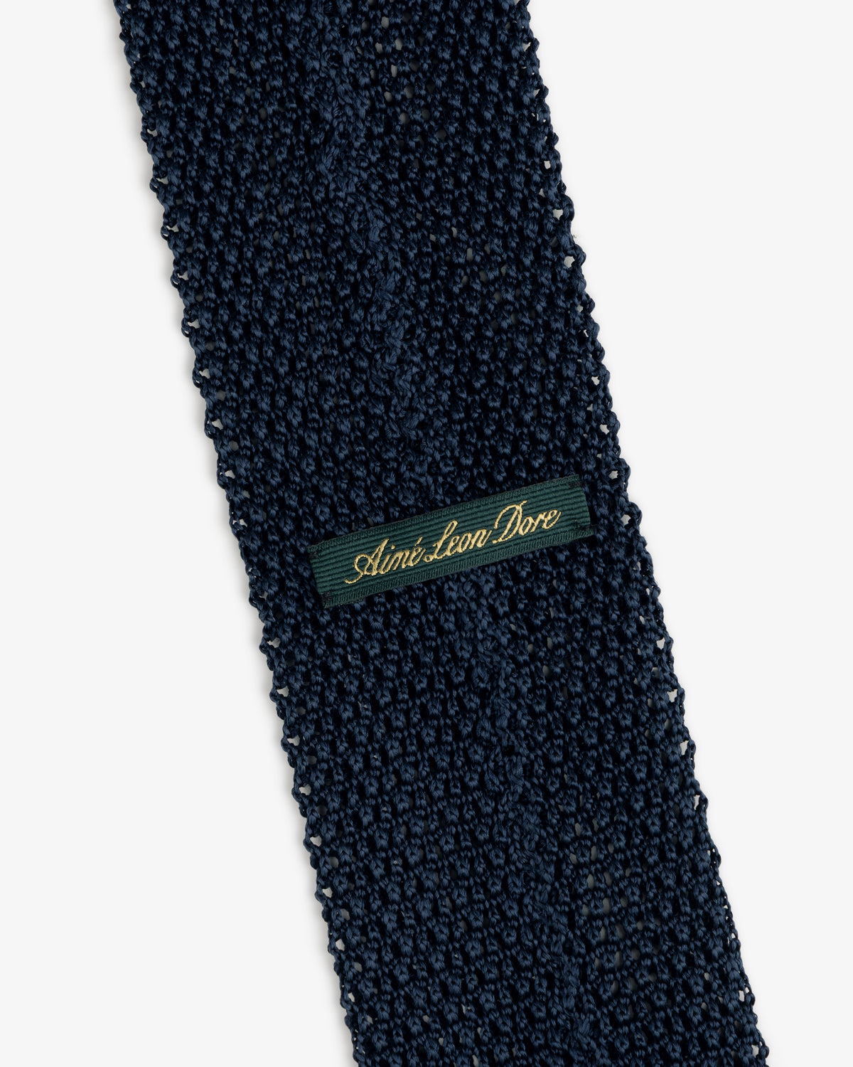 Crest Silk Knit Tie in dark blue, featuring a rectangular green label with gold script embroidery.