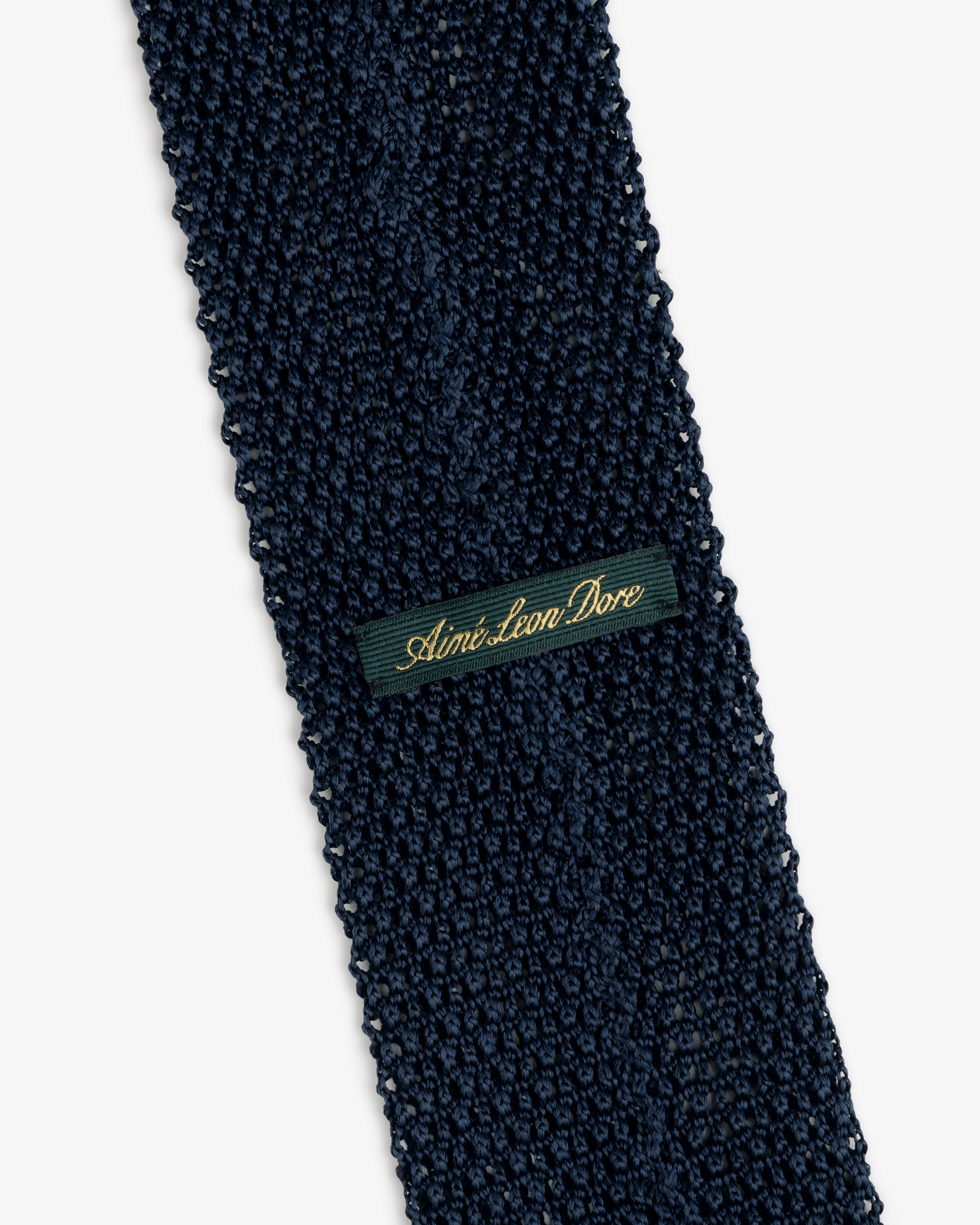 Crest Silk Knit Tie in dark blue, featuring a rectangular green label with gold script embroidery.