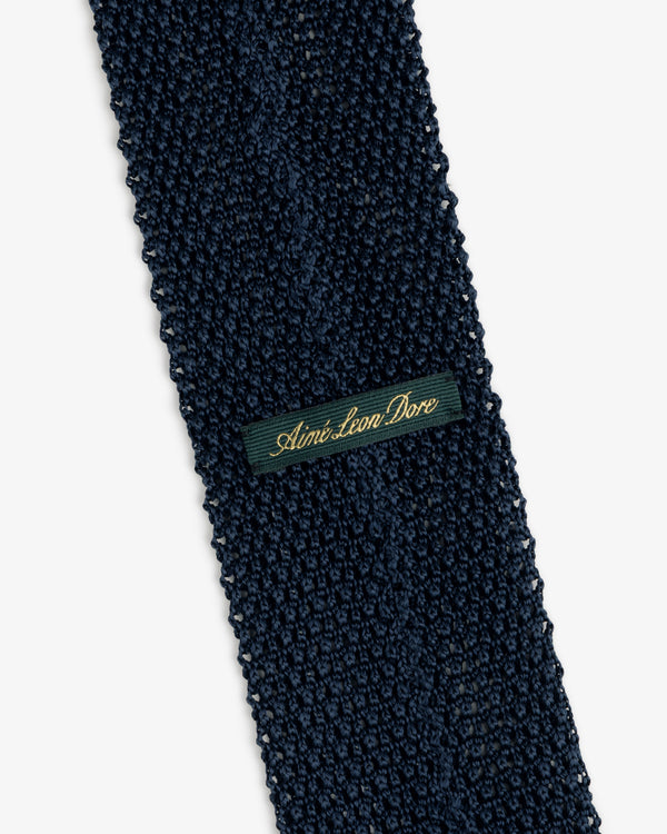 Crest Silk Knit Tie in dark blue, featuring a rectangular green label with gold script embroidery.