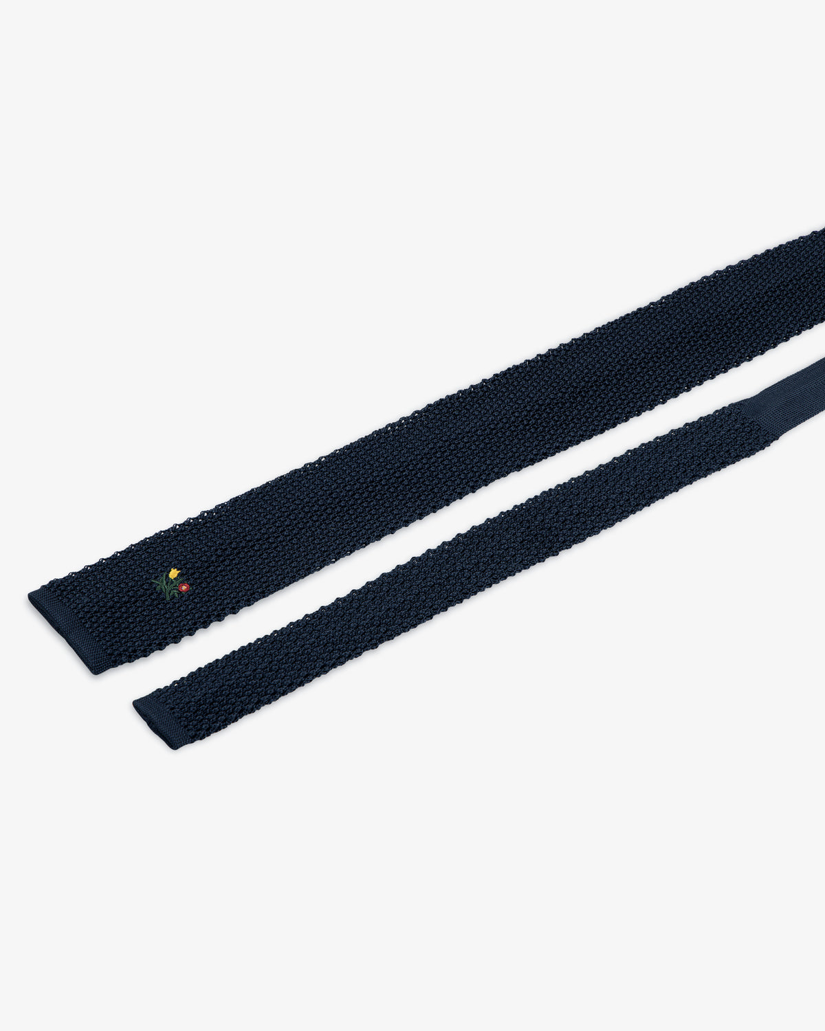 Dark navy blue Crest Silk Knit Tie with a small floral crest embroidered near the end.