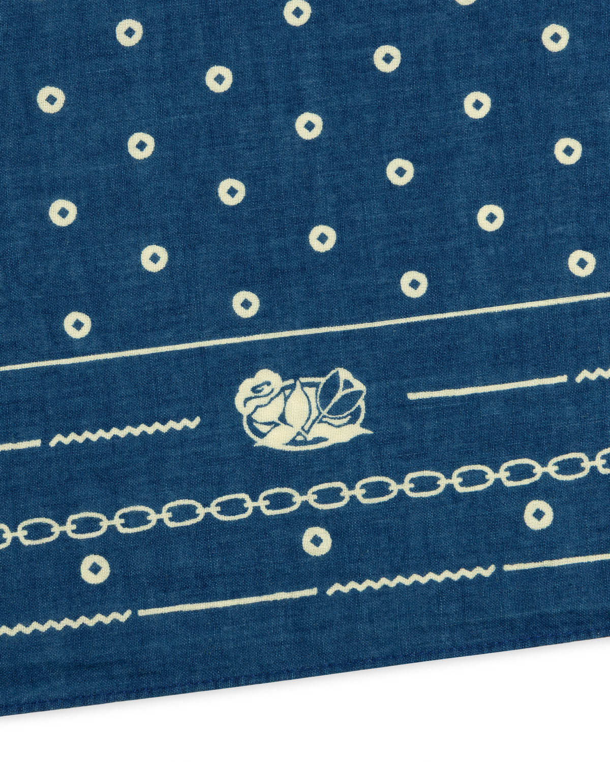 Indigo Dyed Cotton Bandana in blue featuring a white pattern of small circles, a chain link border, and a floral emblem.