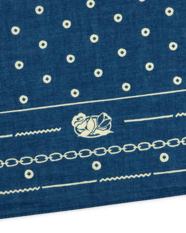 Indigo Dyed Cotton Bandana in blue featuring a white pattern of small circles, a chain link border, and a floral emblem.