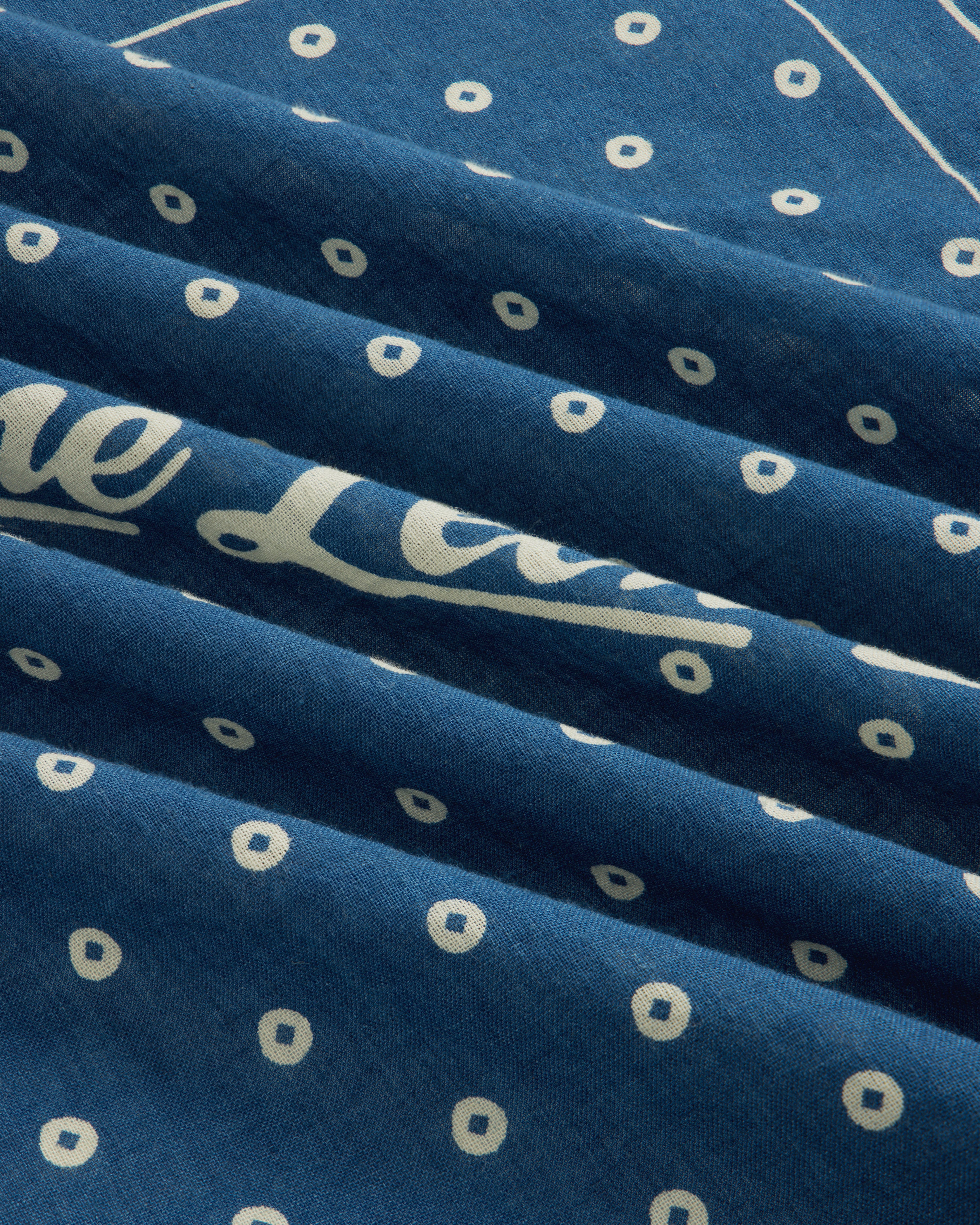 Indigo Dyed Cotton Bandana in blue fabric with a white pattern of small circles and cursive text.