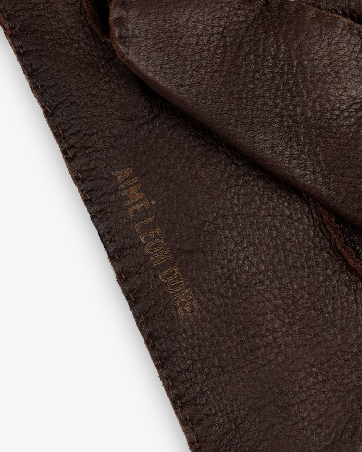 Close-up of brown Henry Gloves with an embossed brand name along the stitched edge.