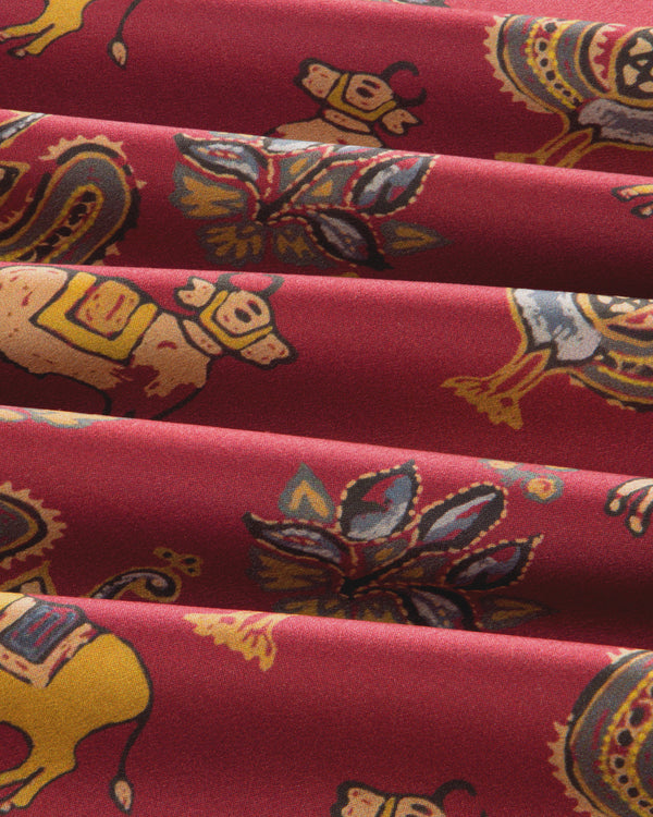 Archival Print Silk Fringe Scarf in red fabric with a repeating print of stylized animals and floral motifs.