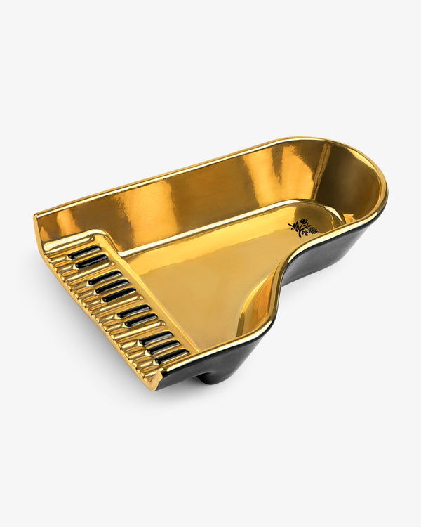 A gold and black Piano Ashtray, shaped like a grand piano with visible keys, on a white background.
