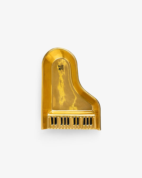 The Piano Ashtray features a shiny gold finish and a grand piano shape with black and white keys at the bottom.