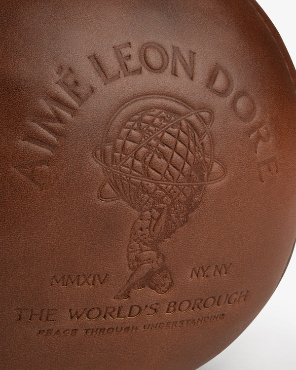 Brown leather surface of an Atlas Vintage Leather 10 Lb Kettle Bell embossed with a figure holding a globe and text.