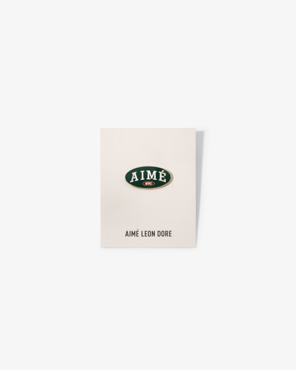 A white card with an oval Graphic Pin reading AIMÉ in green/gold, AIMÉ LEON DORE printed below.