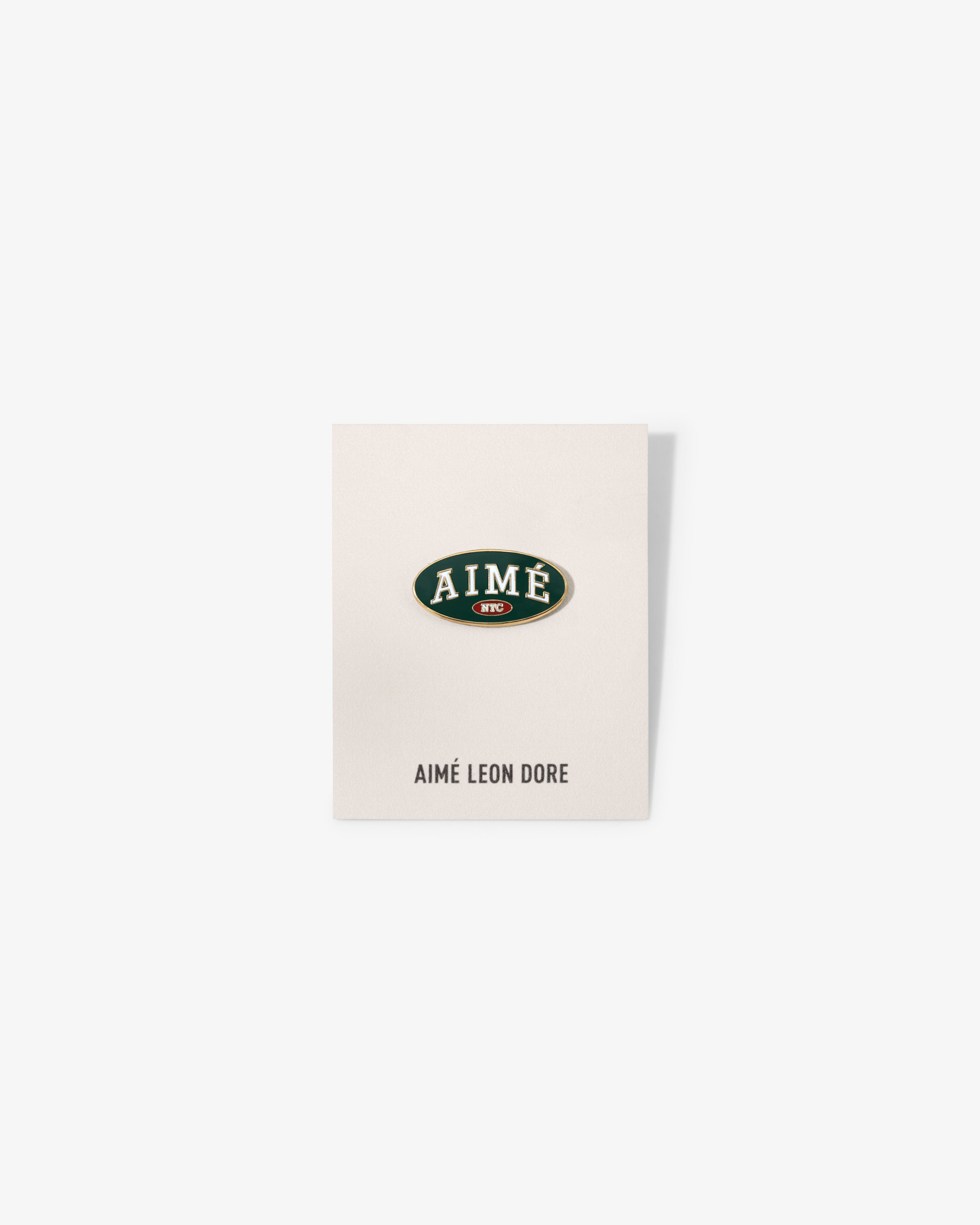 A white card with an oval Graphic Pin reading AIMÉ in green/gold, AIMÉ LEON DORE printed below.