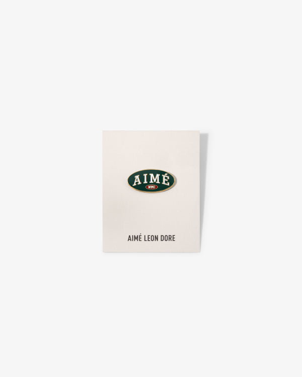 A white card with an oval Graphic Pin reading AIMÉ in green/gold, AIMÉ LEON DORE printed below.