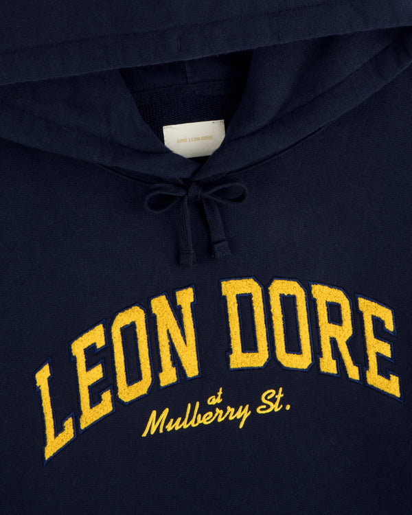 Mulberry Letterman Hoodie: Navy with LEON DORE in yellow and “at Mulberry St.” cursive below.