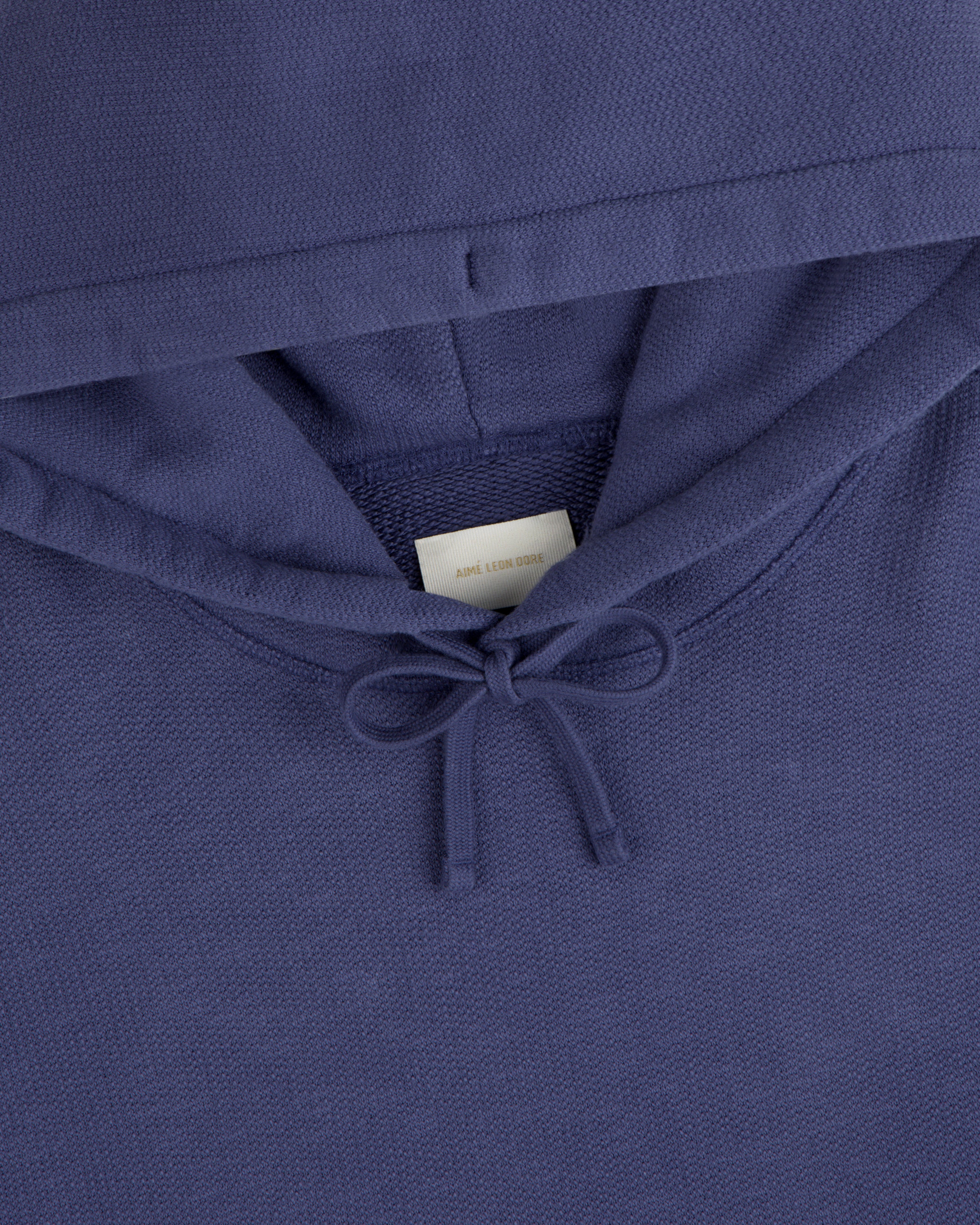 Close-up of the Stone Washed Marina Hoodie in purple, featuring a drawstring and visible white neck tag.