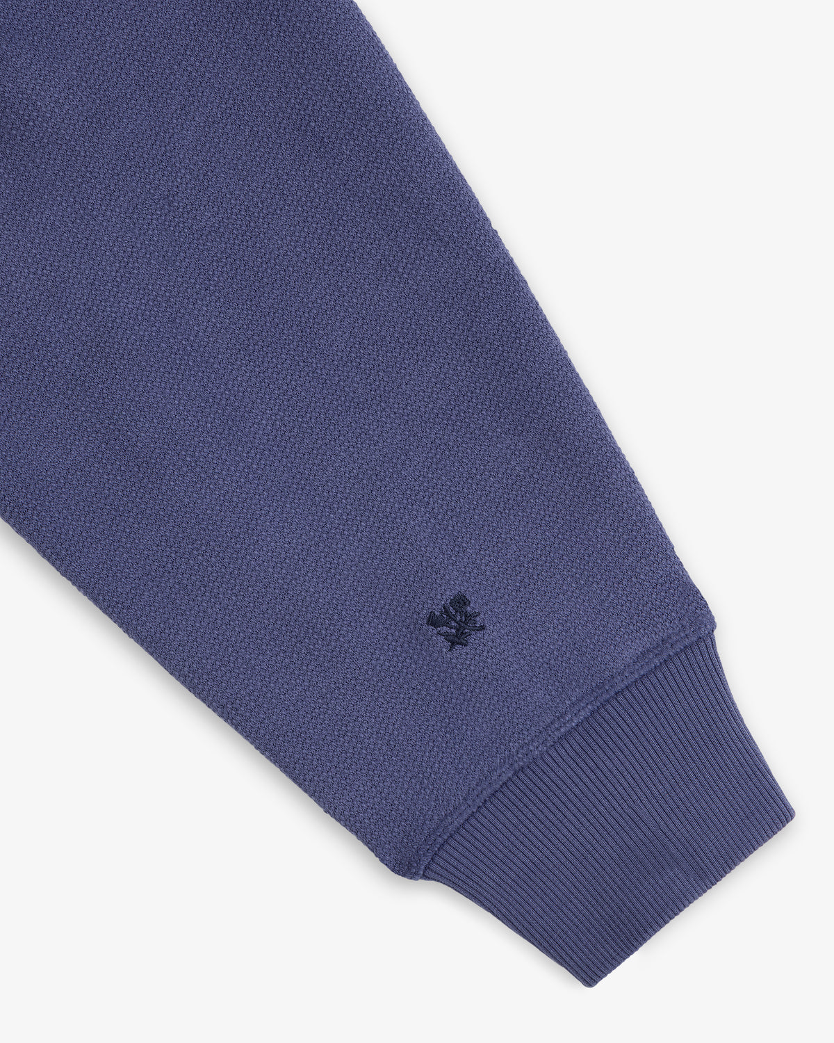 A close-up of the Stone Washed Marina Hoodie’s blue textured sleeve, ribbed cuff, and stitched dark blue wrist logo.
