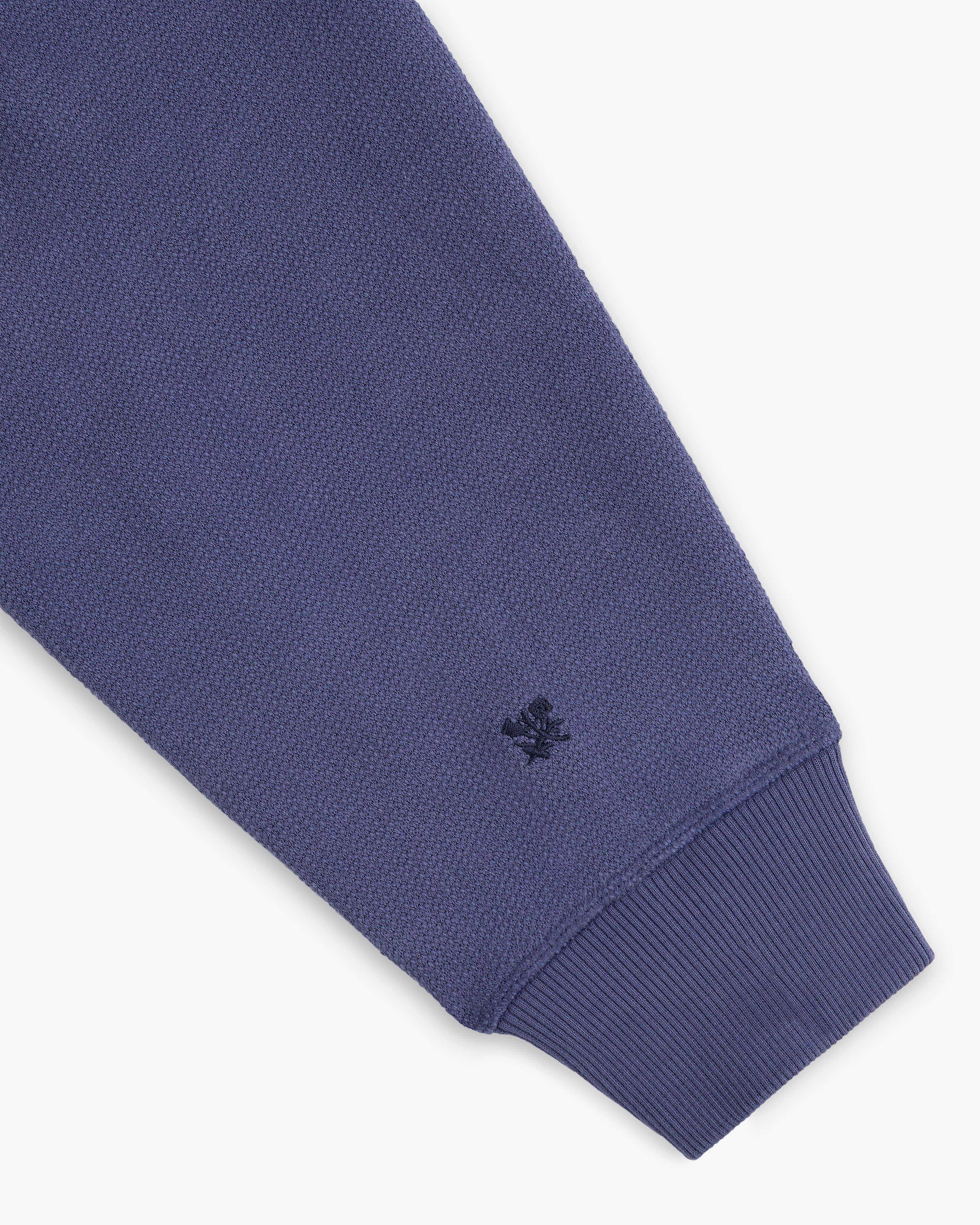 A close-up of the Stone Washed Marina Hoodie’s blue textured sleeve, ribbed cuff, and stitched dark blue wrist logo.